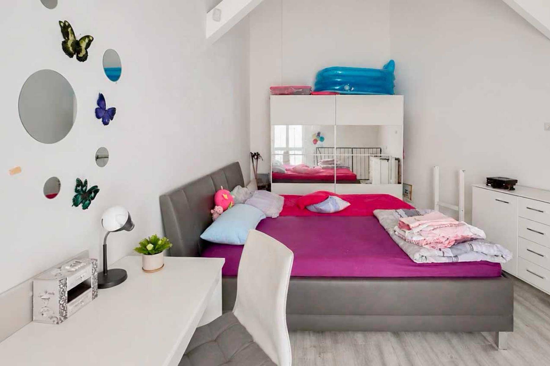 Helles Schlafzimmer mit Dachschräge, Bett, Schreibtisch und Spiegelschrank, dekoriert mit Schmetterlingen.