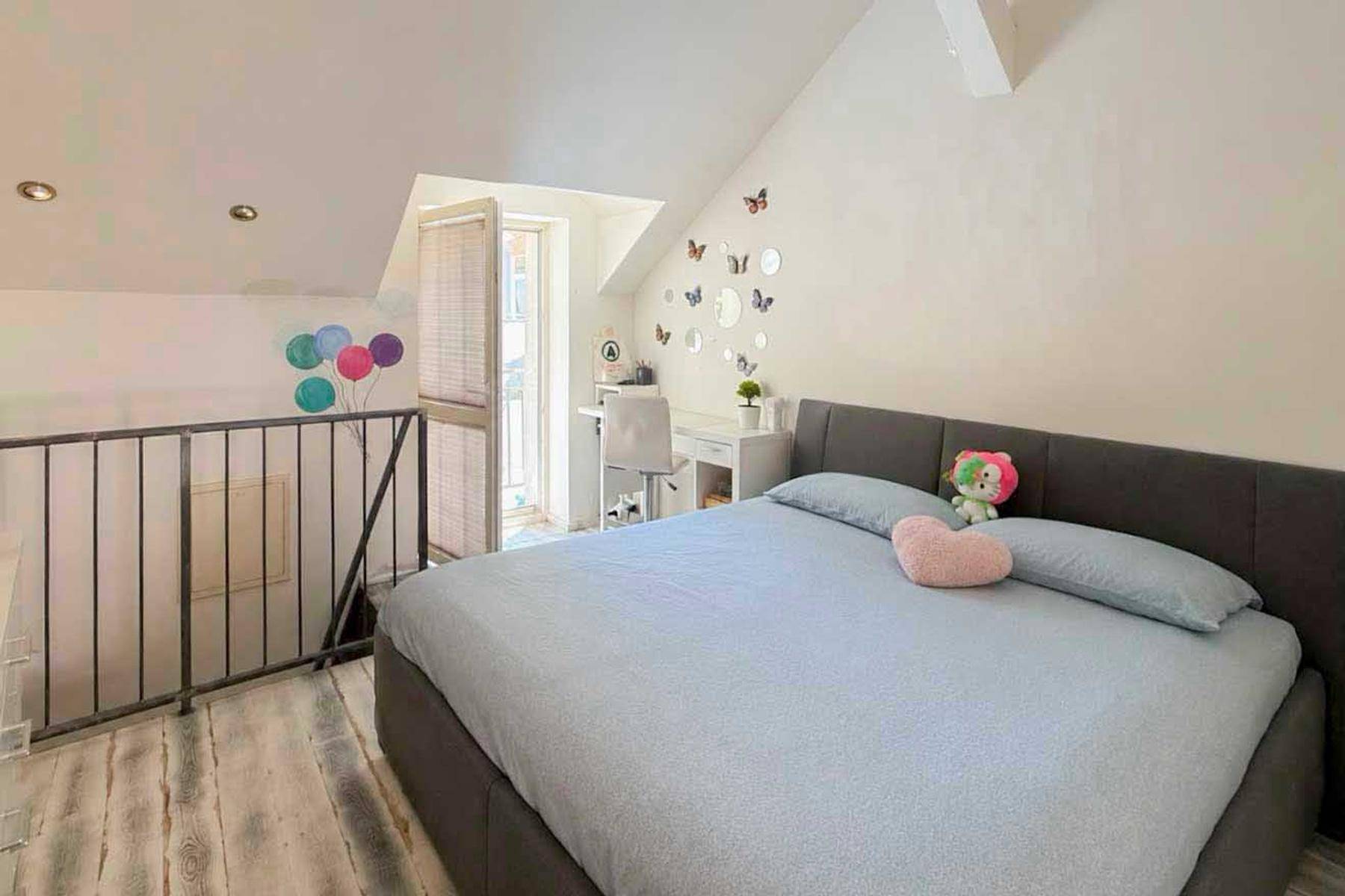 Schlafzimmer im Dachgeschoss mit Bett, Schreibtisch und Blick auf den unteren Bereich durch ein offenes Fenster.