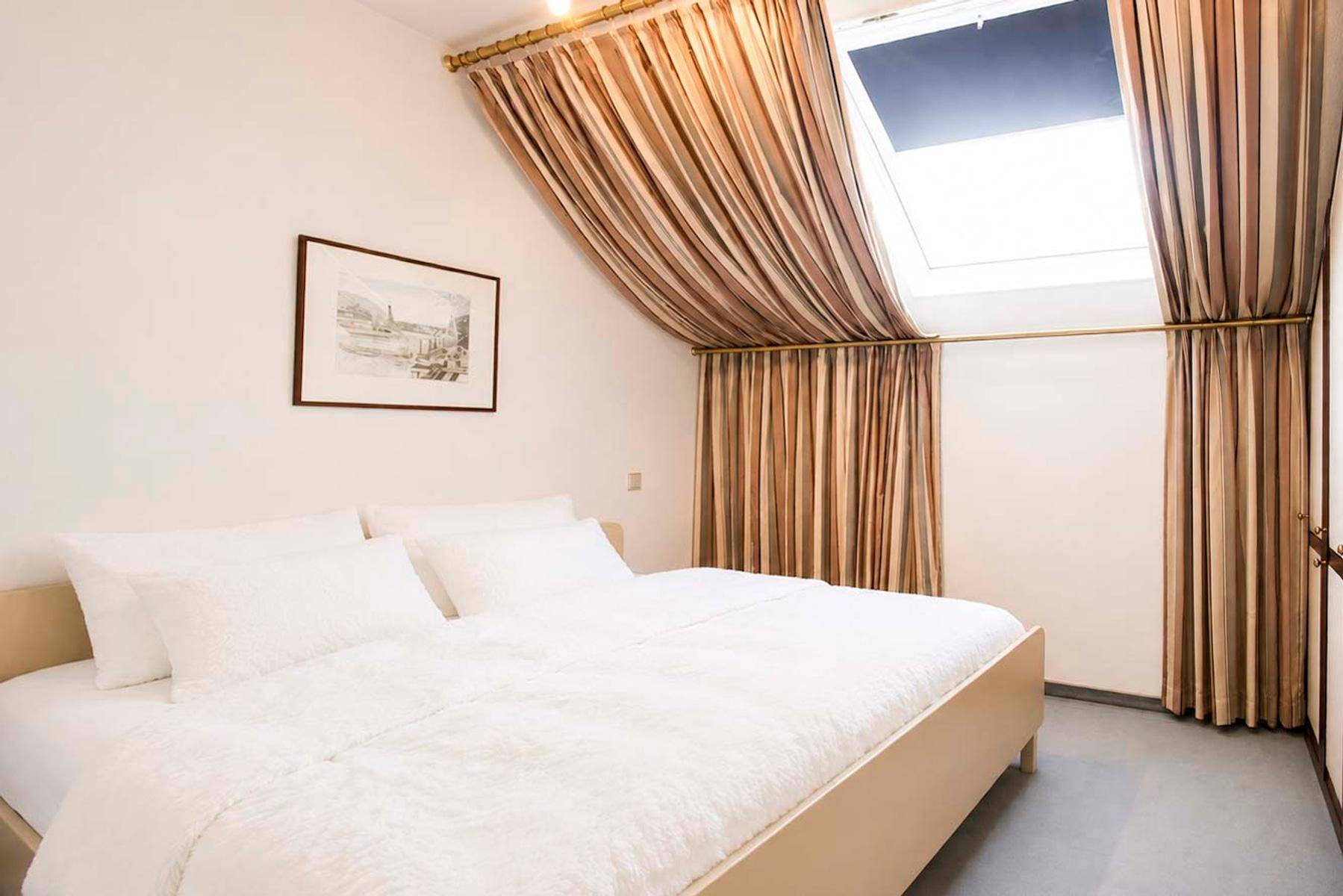 Schlafzimmer im Dachgeschoss mit Doppelbett, Dachfenster und gestreiften Vorhängen für viel Licht.