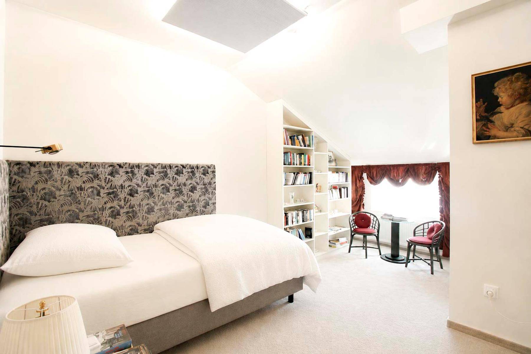 Helles Schlafzimmer mit Einzelbett, Bücherregalen und schrägen Wänden im charmanten Dachgeschoss.