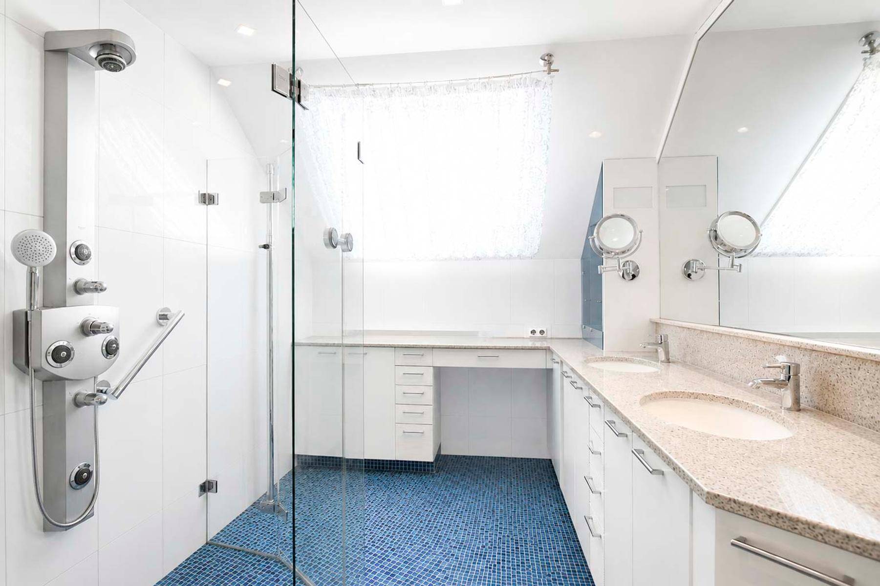Modernes Badezimmer mit begehbarer Dusche, Doppelwaschbecken und blauen Mosaikfliesen am Boden.
