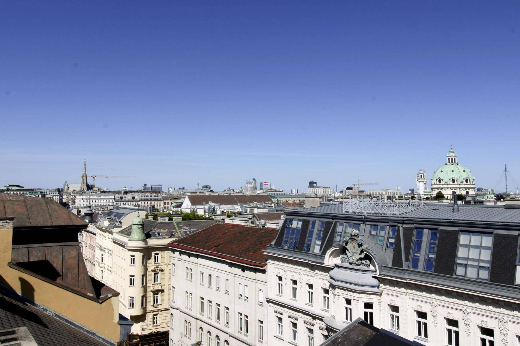 Weitläufiger Stadtblick über historische Dächer mit markanter Kuppel und moderner Skyline im Hintergrund.