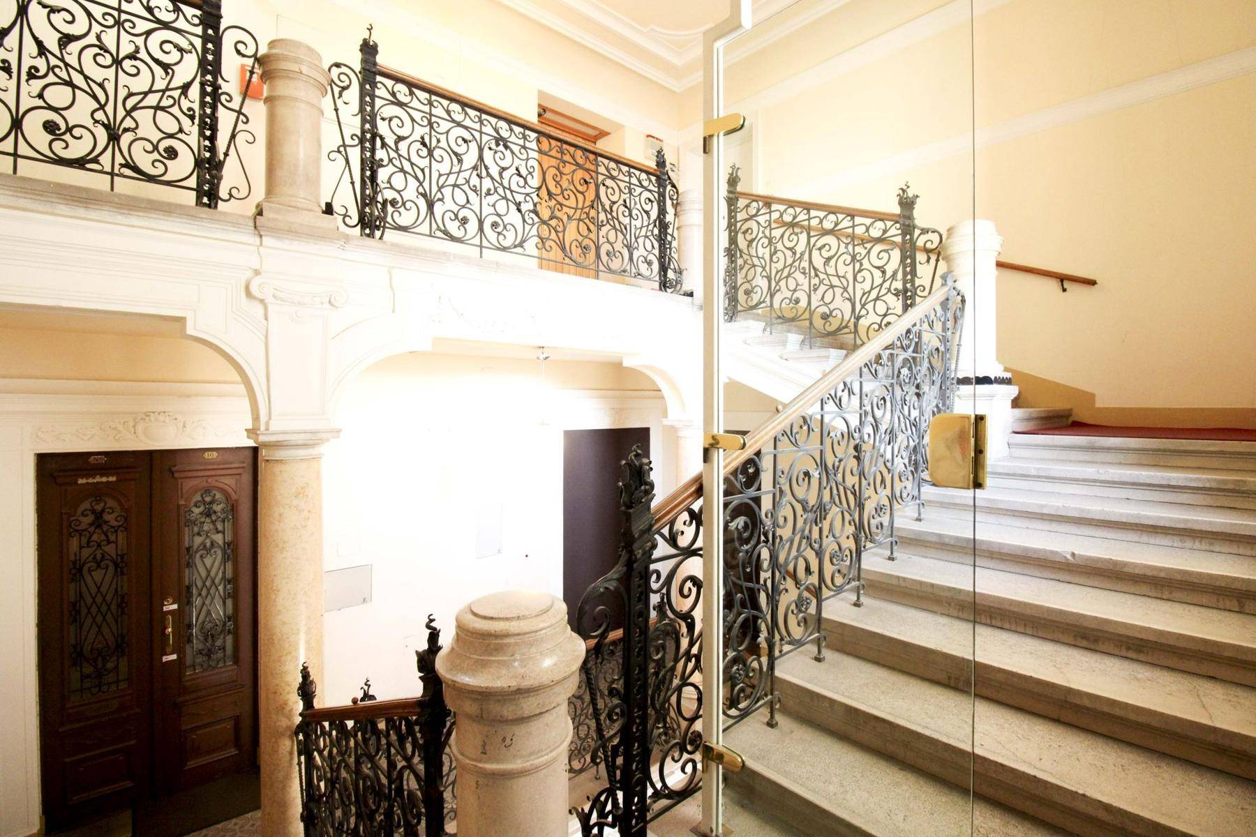 Elegantes Treppenhaus mit schmiedeeisernen Geländern, Steinstufen und modernem Glasaufzug.
