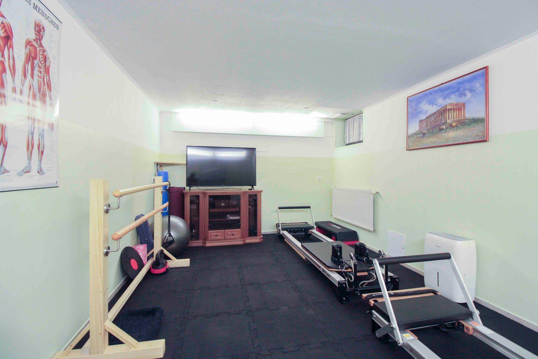 Fitnessraum im Untergeschoss mit Trainingsgeräten, Fernseher und Gummiboden.