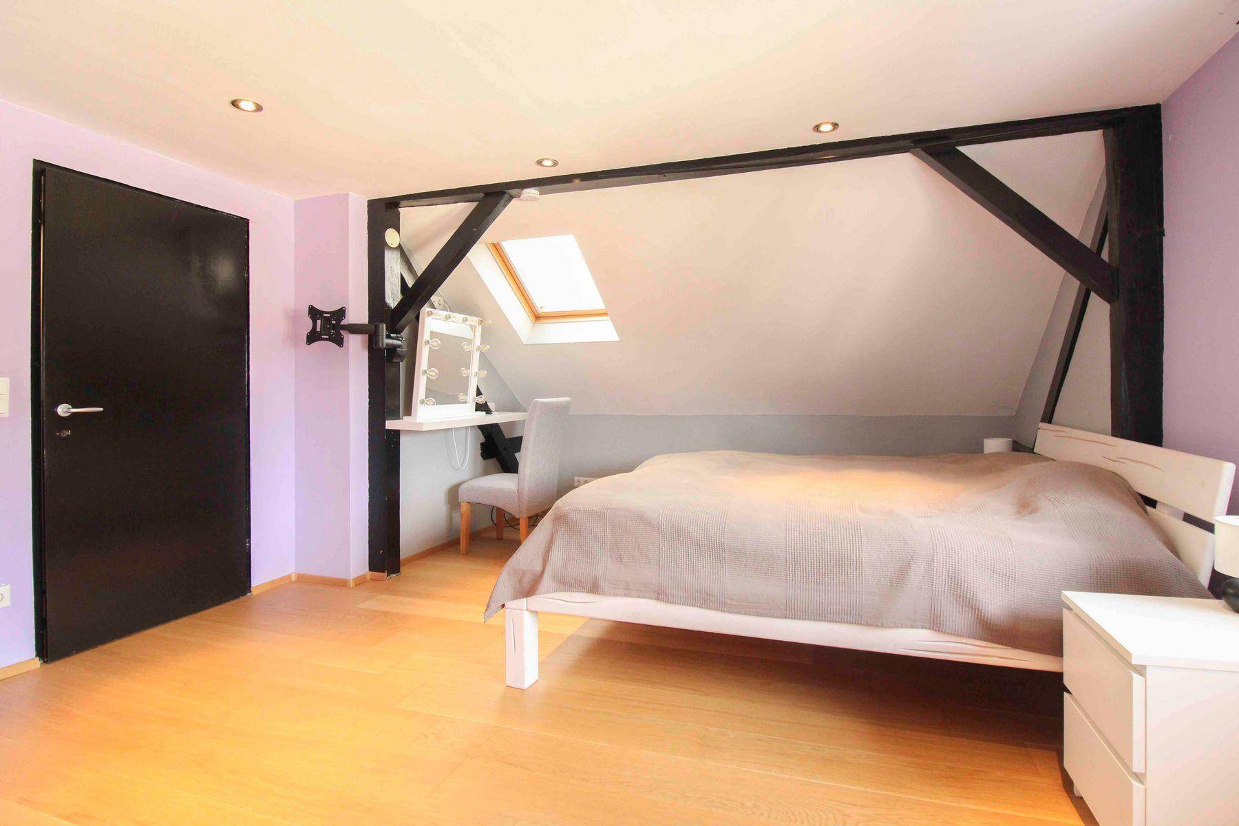 Dachgeschoss-Schlafzimmer mit Schminktisch, Dachfenster und dunklen Holzbalken.