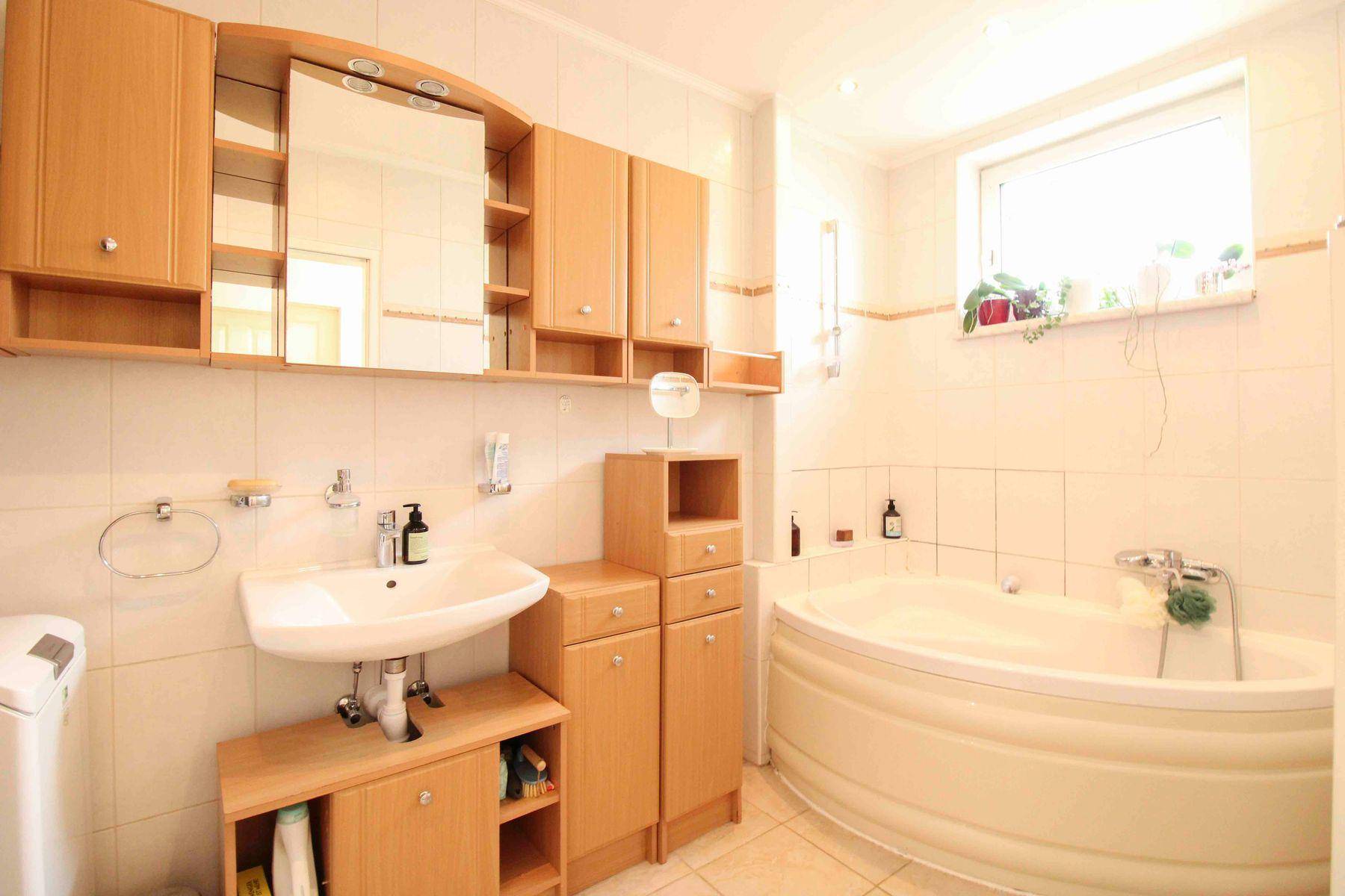 Badezimmer mit Eckbadewanne, Einzelwaschbecken und hellen Holzschränken.