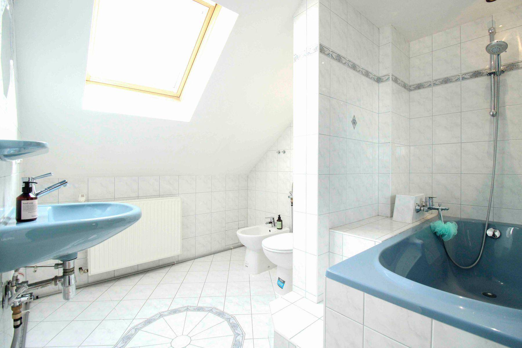 Dachgeschoss-Badezimmer mit blauer Badewanne, Waschbecken, Bidet und Dachfenster.