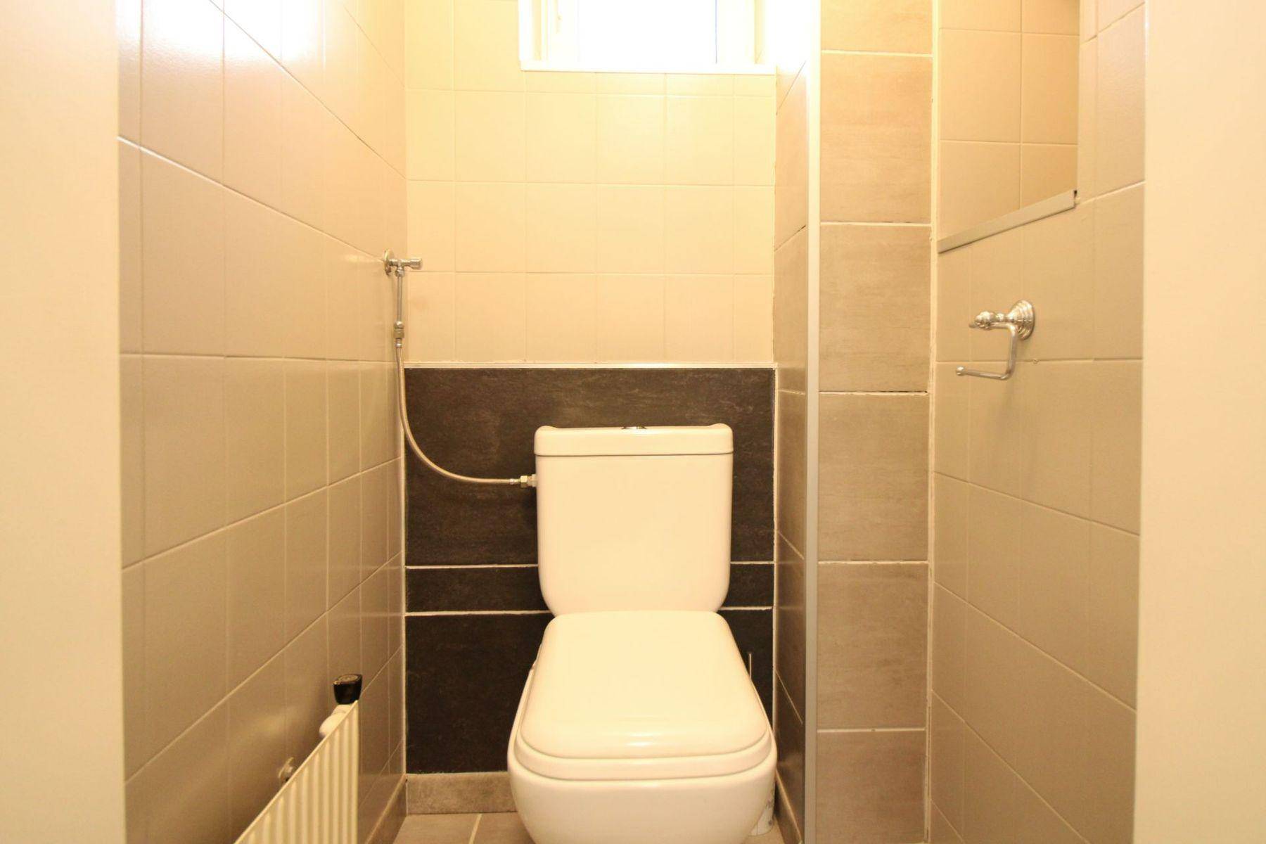 Kleines WC mit Toilette und Bidet-Duschfunktion, gefliest in neutralen Farben.