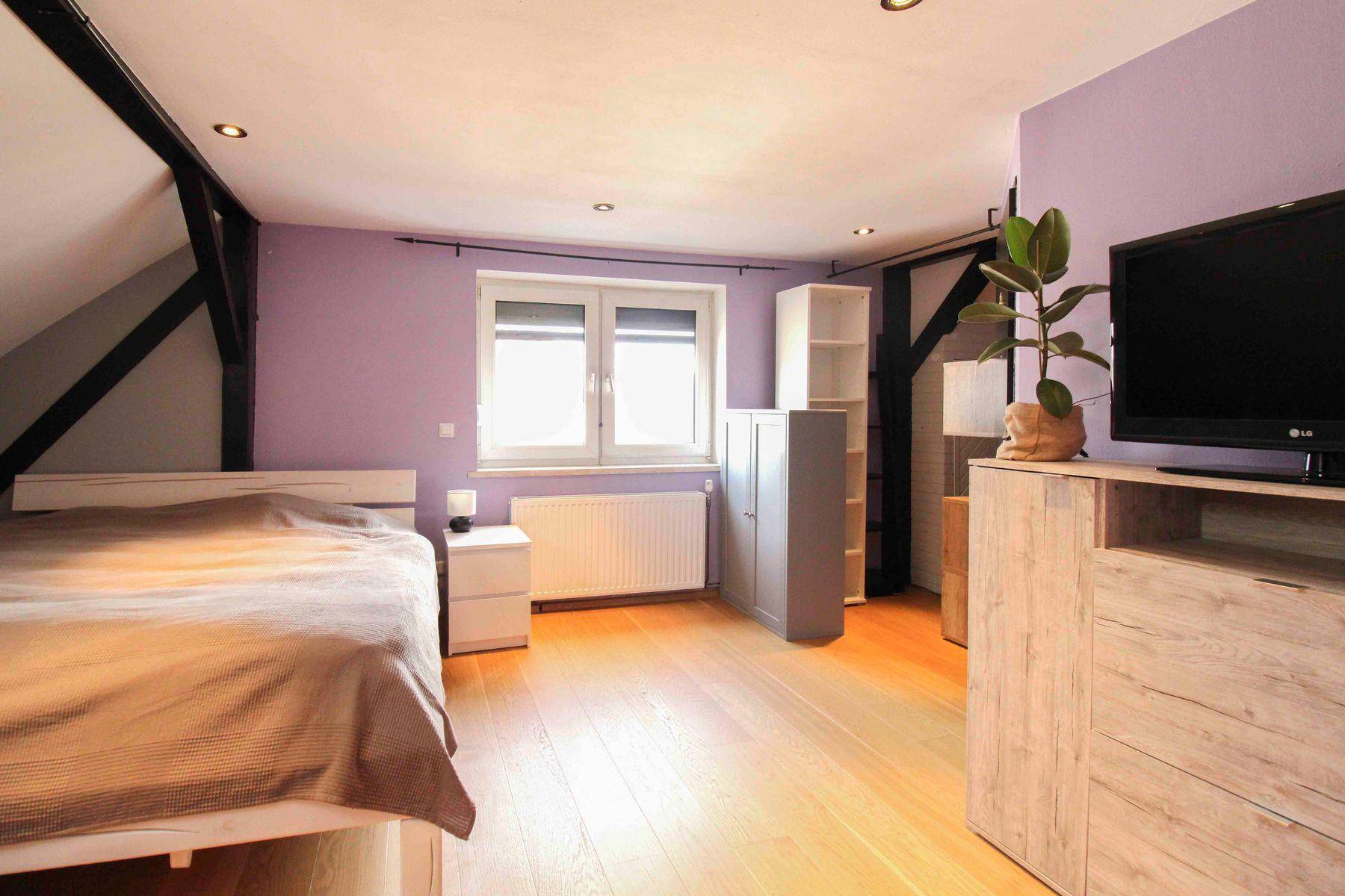 Schlafzimmer im Dachgeschoss mit lila Wänden, sichtbaren Holzbalken und Dachfenster.