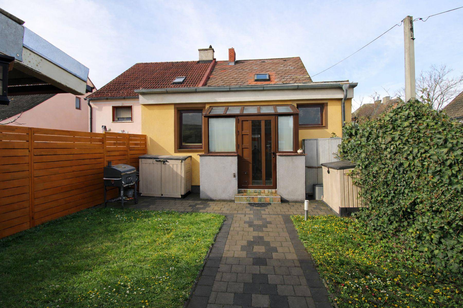 Kleiner Gartenbereich hinter dem Haus mit Rasenfläche, gepflastertem Weg und Grillplatz.