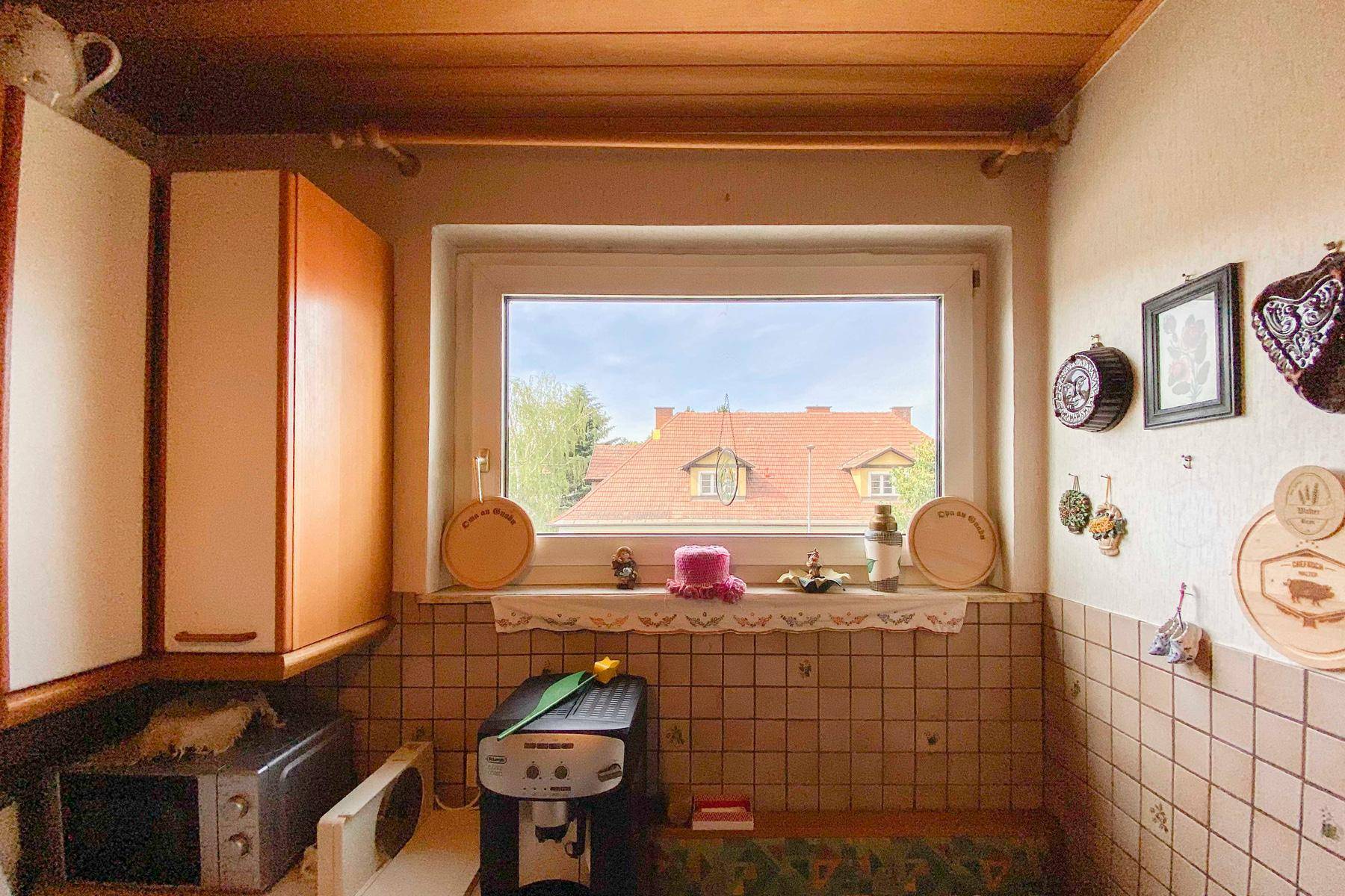 Kleine Küche mit Fenster, Fliesen und Blick auf die Dächer der Nachbarschaft.