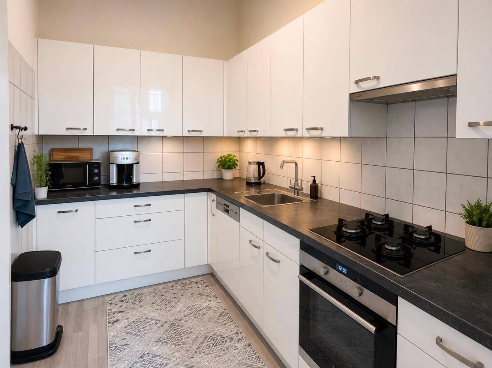 Moderne weiße Küche mit Hochglanzfronten, dunkler Arbeitsplatte und integrierten Geräten.