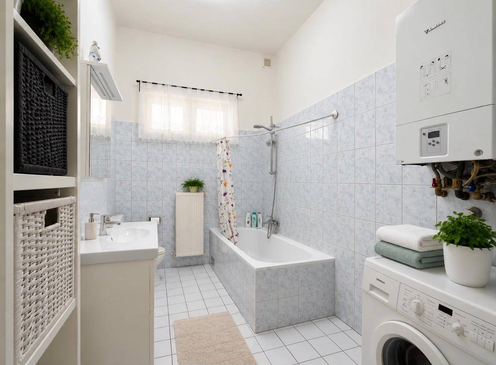 Gefliestes Badezimmer mit Badewanne, Waschbecken, Waschmaschine und Wandheizkessel.