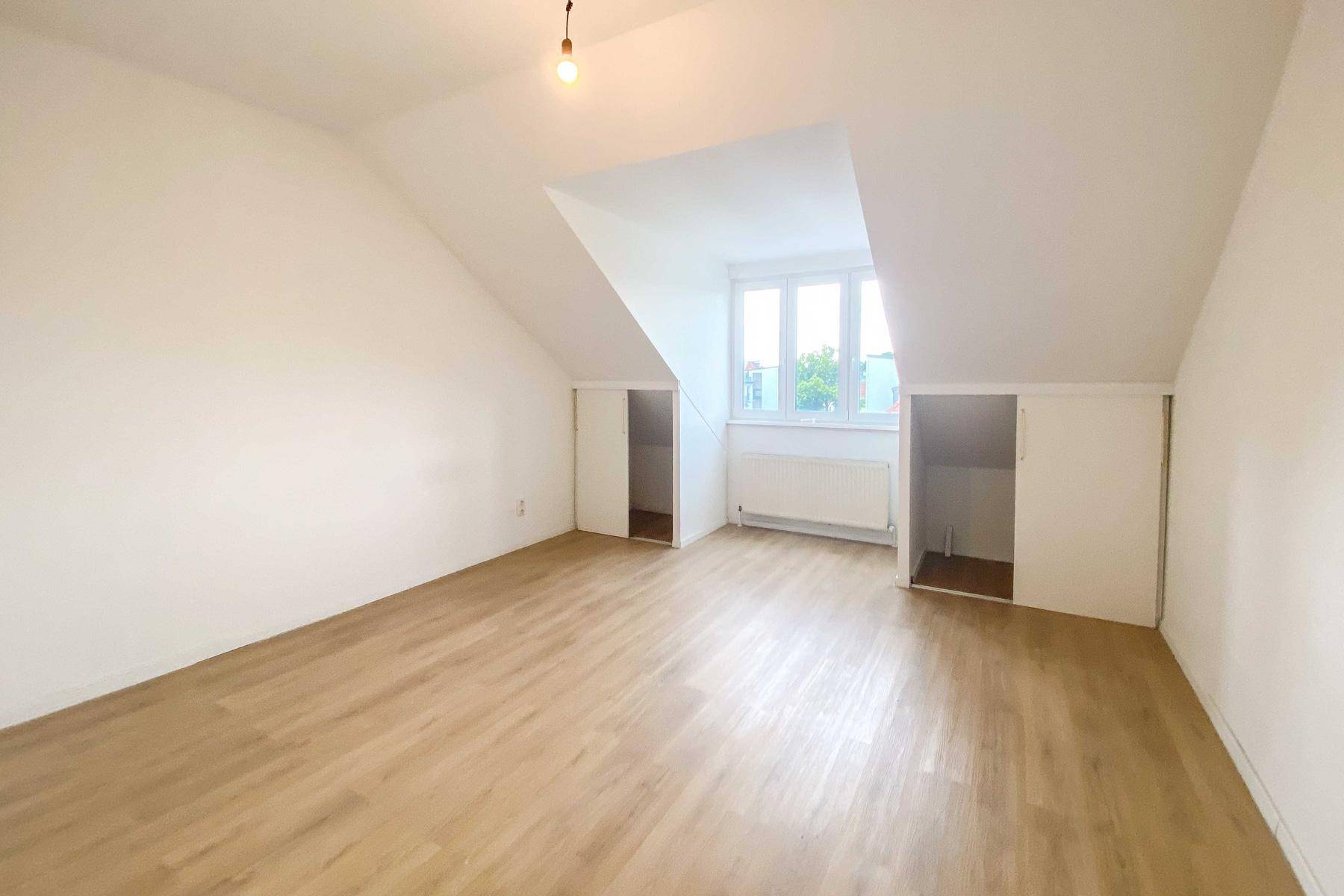 Leeres Zimmer mit Dachschrägen, großem Fenster und praktischen Einbauschränken.