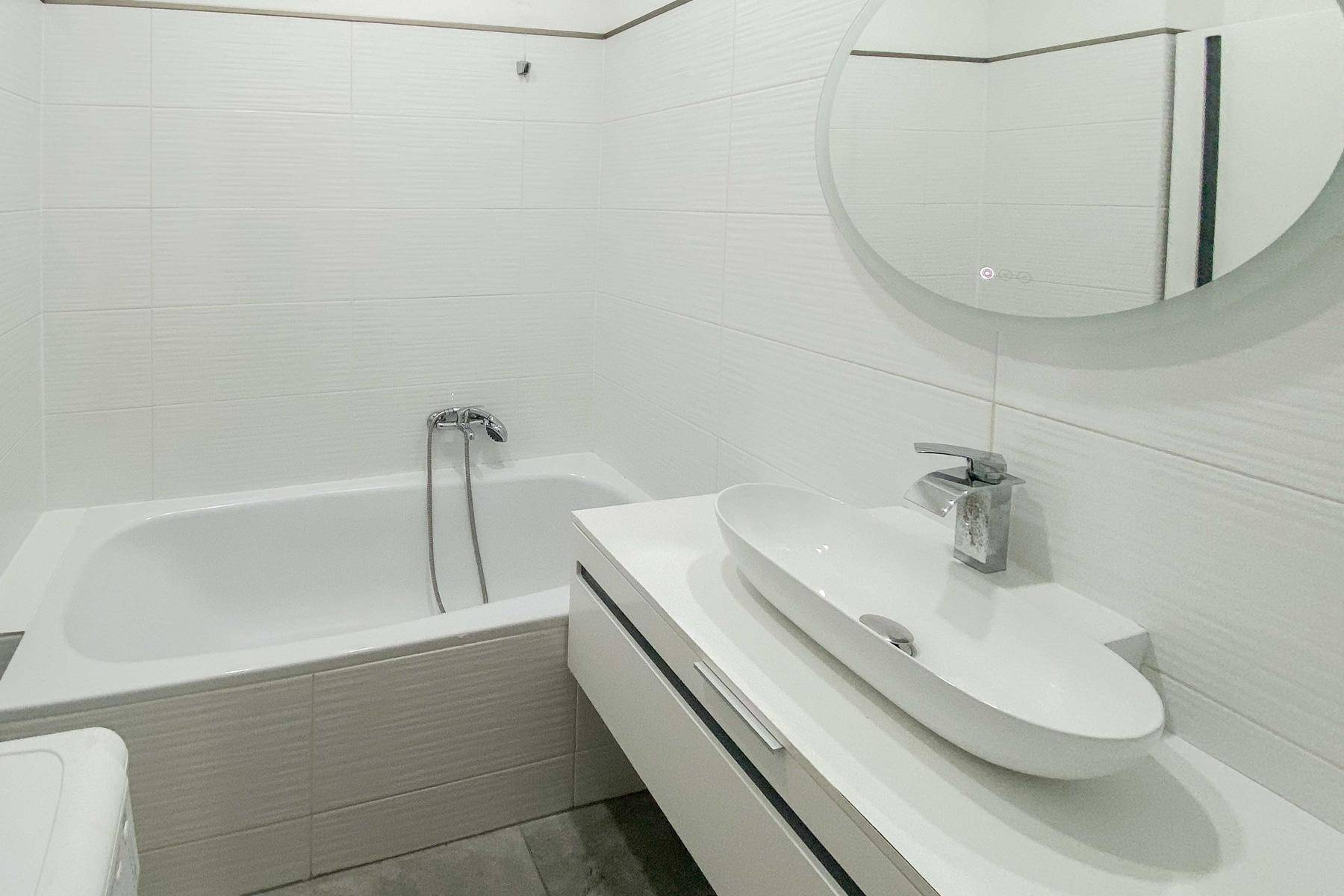 Modernes Badezimmer mit Badewanne, elegantem Waschbecken und rundem Spiegel.