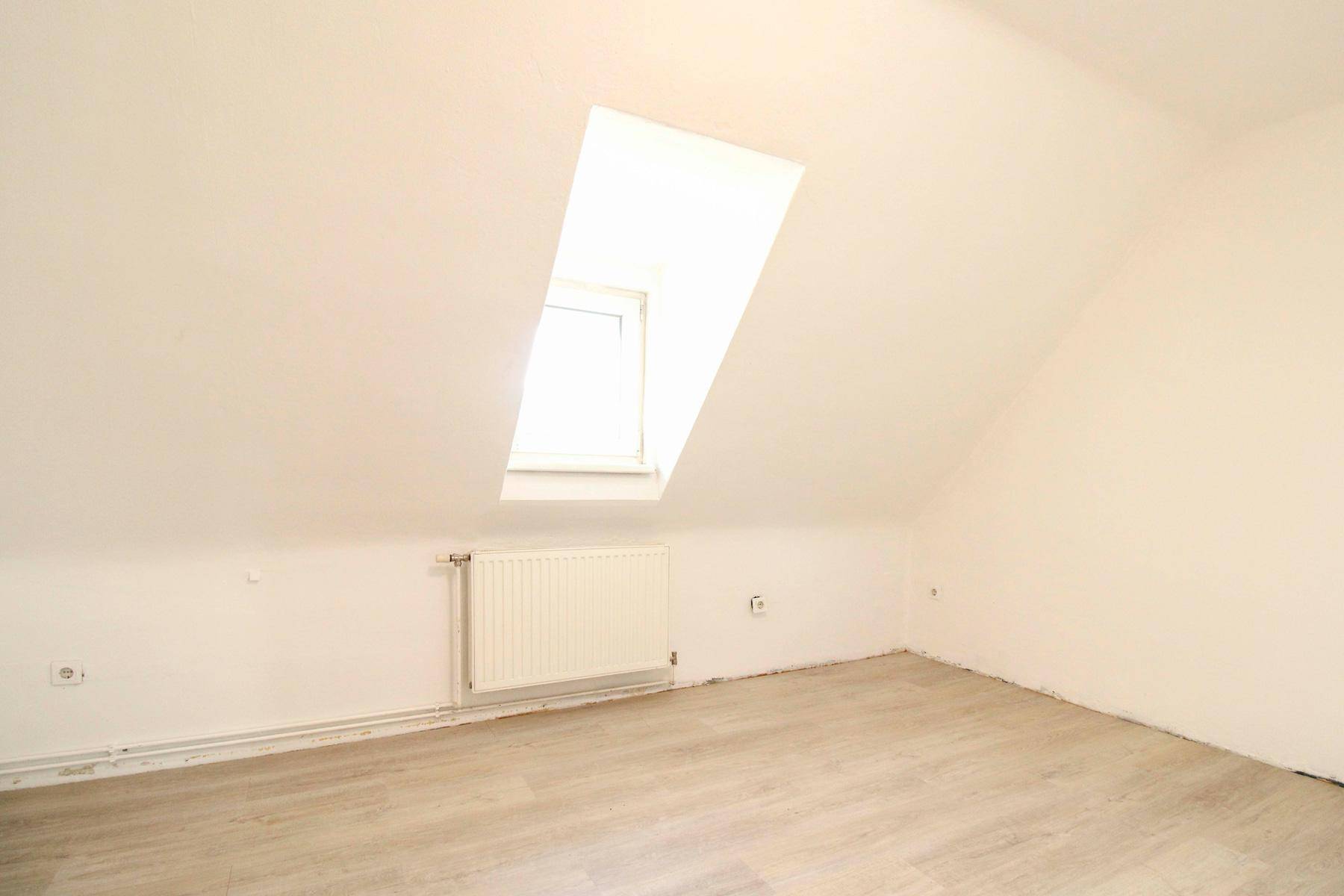 Heller Dachbodenraum mit schräger Decke, Dachfenster und Heizkörper.