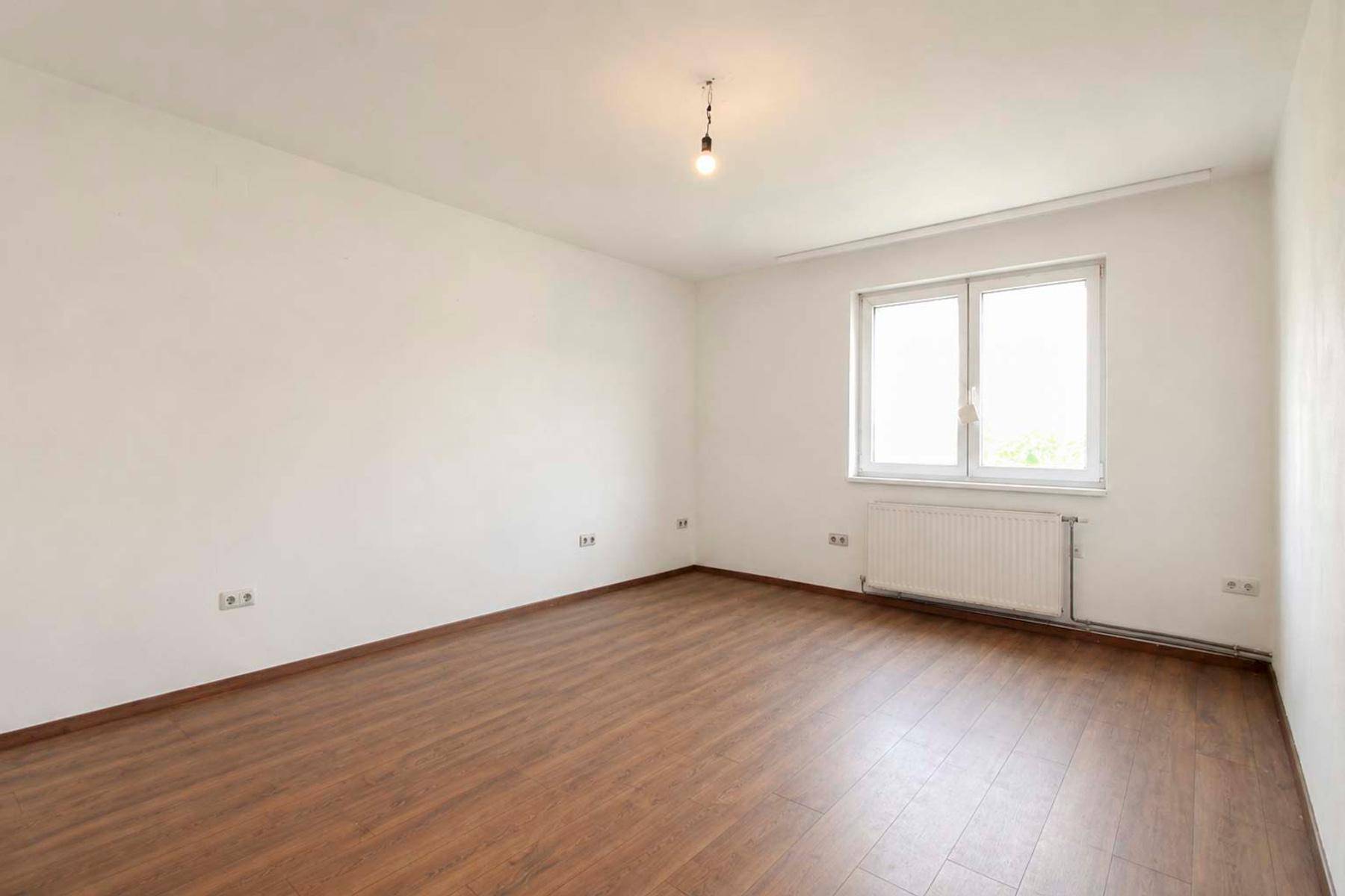 Heller, leerer Raum mit weiß gestrichenen Wänden und Laminatboden.