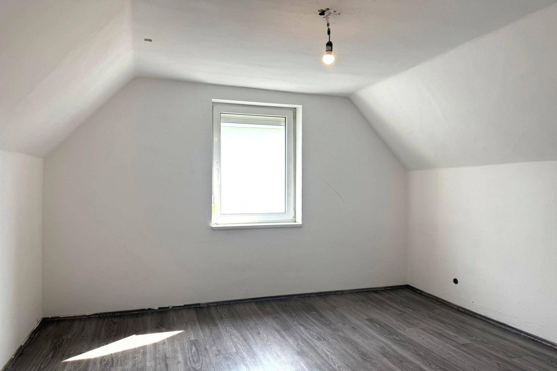 Dachbodenraum mit schrägen Wänden, Fenster und dunklem Laminatboden.