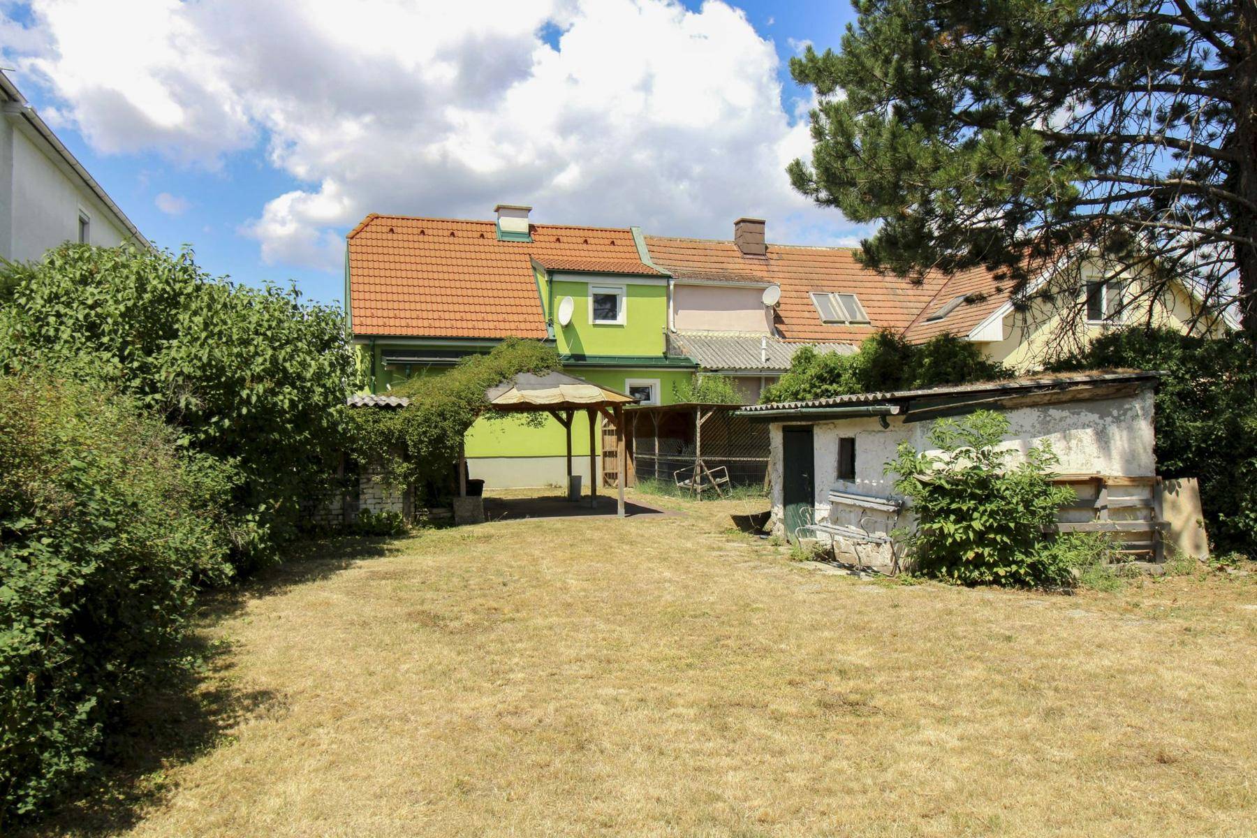 Großer Gartenbereich hinter dem Haus mit Rasenfläche, Gartenlaube und Schuppen.