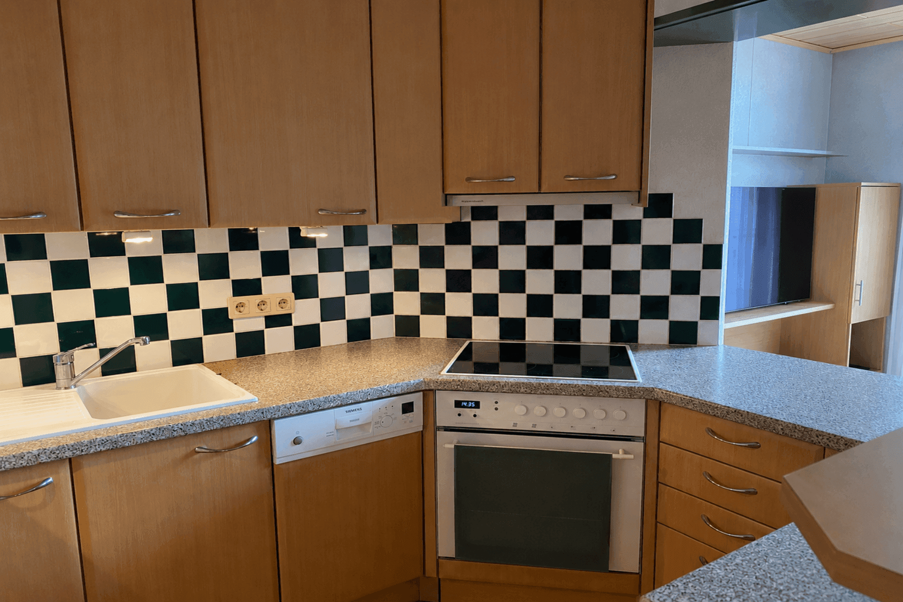 Funktionale Küche mit hellen Holzschränken, Granit-Arbeitsplatte und markanter schwarz-weißer Fliesenrückwand.
