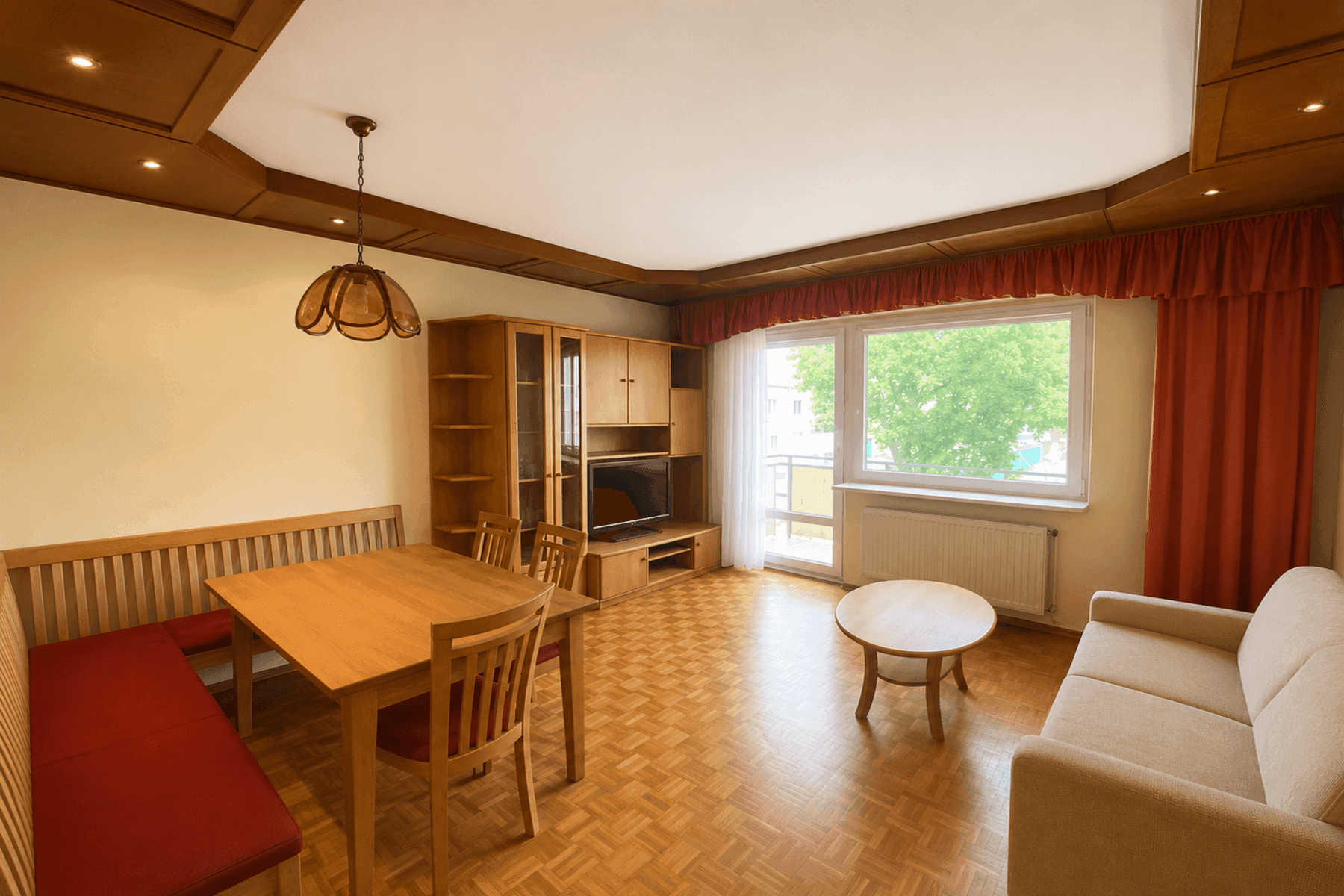 Gemütlicher Wohn- und Essbereich mit Holzmöbeln, Parkettboden und Zugang zum Balkon.