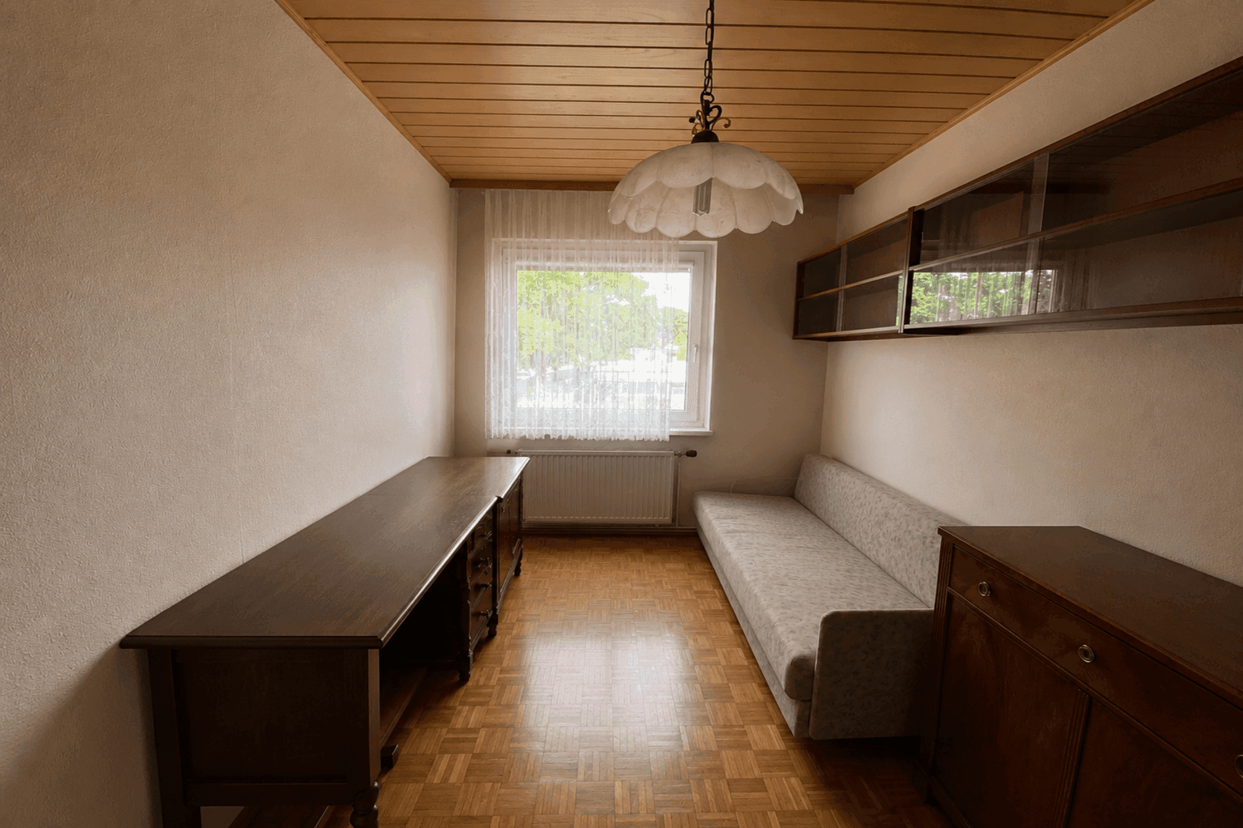 Möbliertes Zimmer mit Parkettboden, Holzdecke und Fenster, ideal als Schlaf- oder Arbeitszimmer.
