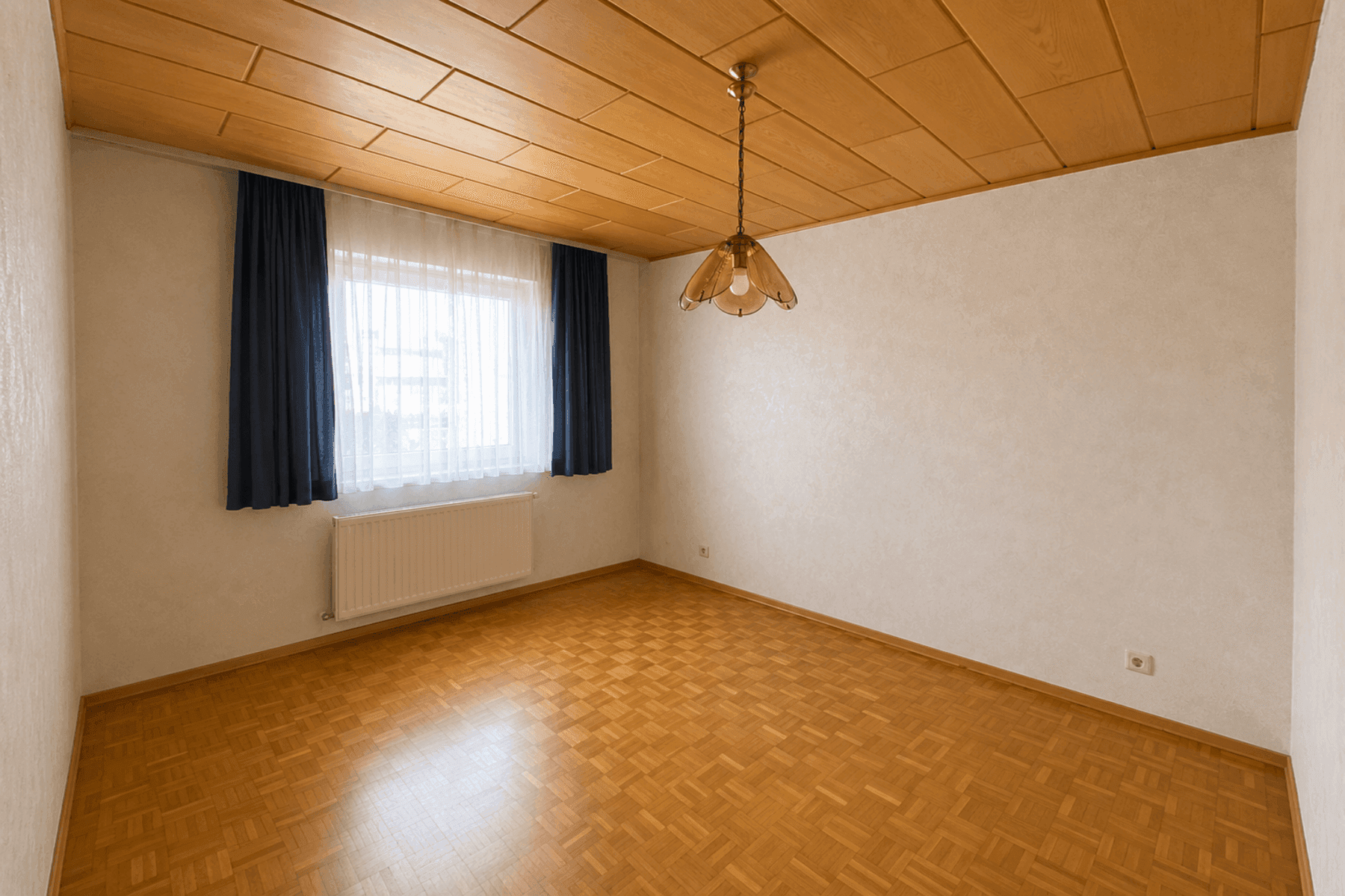 Leeres Zimmer mit Parkettboden, Holzdecke und Fenster mit blauen Vorhängen.