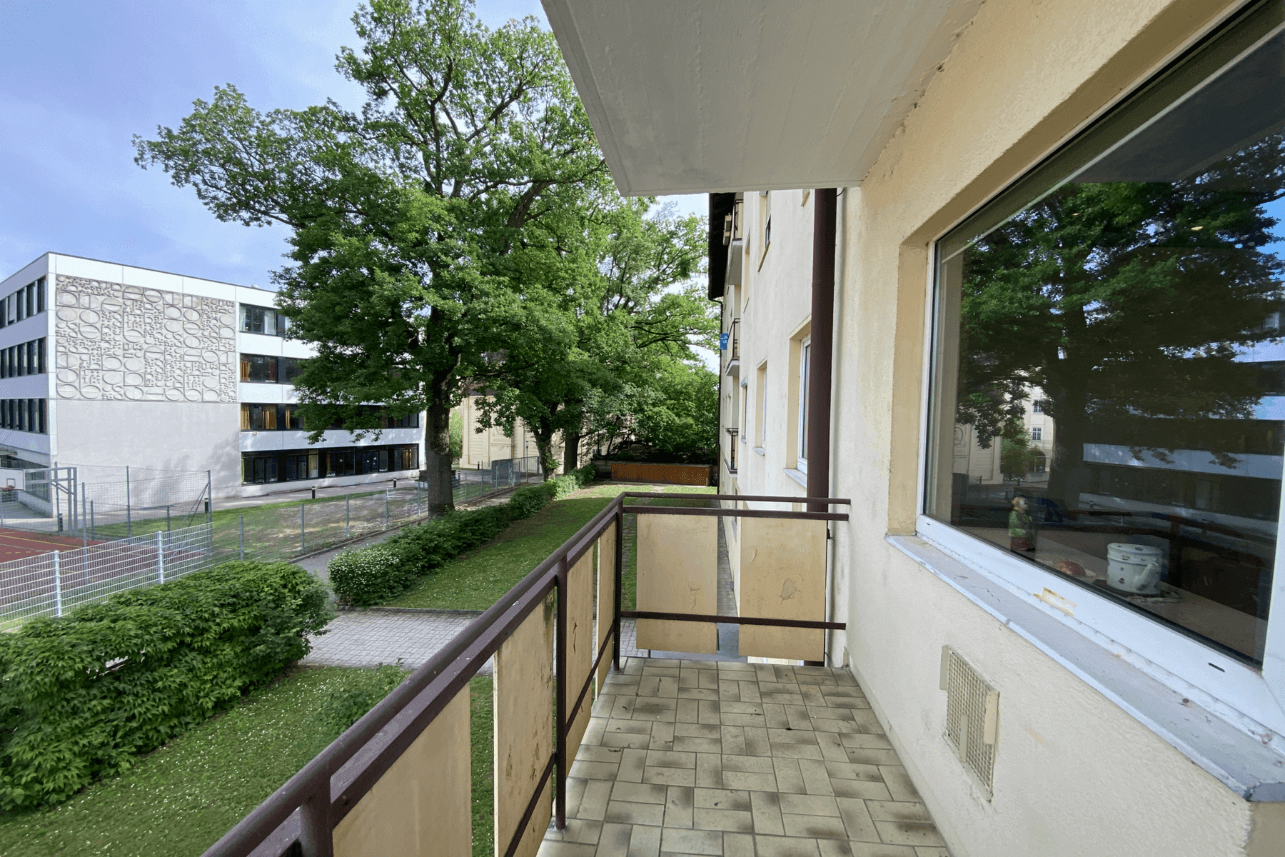 Balkon mit Fliesenboden und Blick auf grüne Bäume und ein angrenzendes Gebäude.