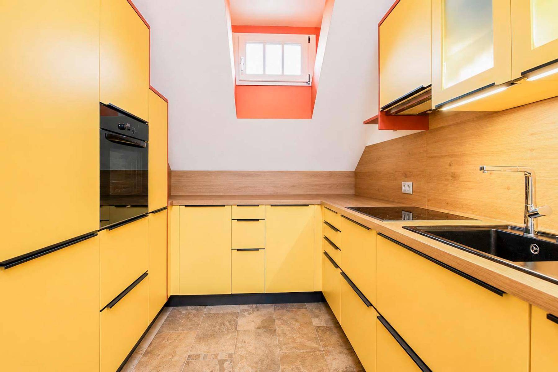 Moderne Küche mit gelben Fronten, Dachfenster und integrierten Geräten unter Dachschräge.