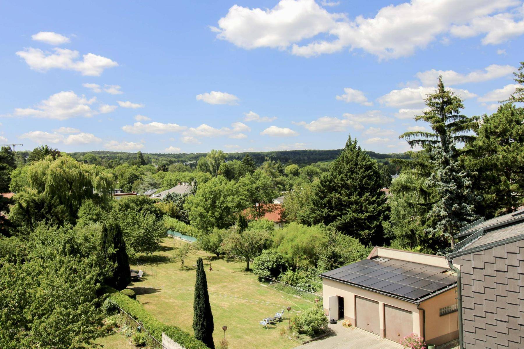 Weitläufiger Gartenbereich mit Rasenfläche, Bäumen und Blick auf die Umgebung.