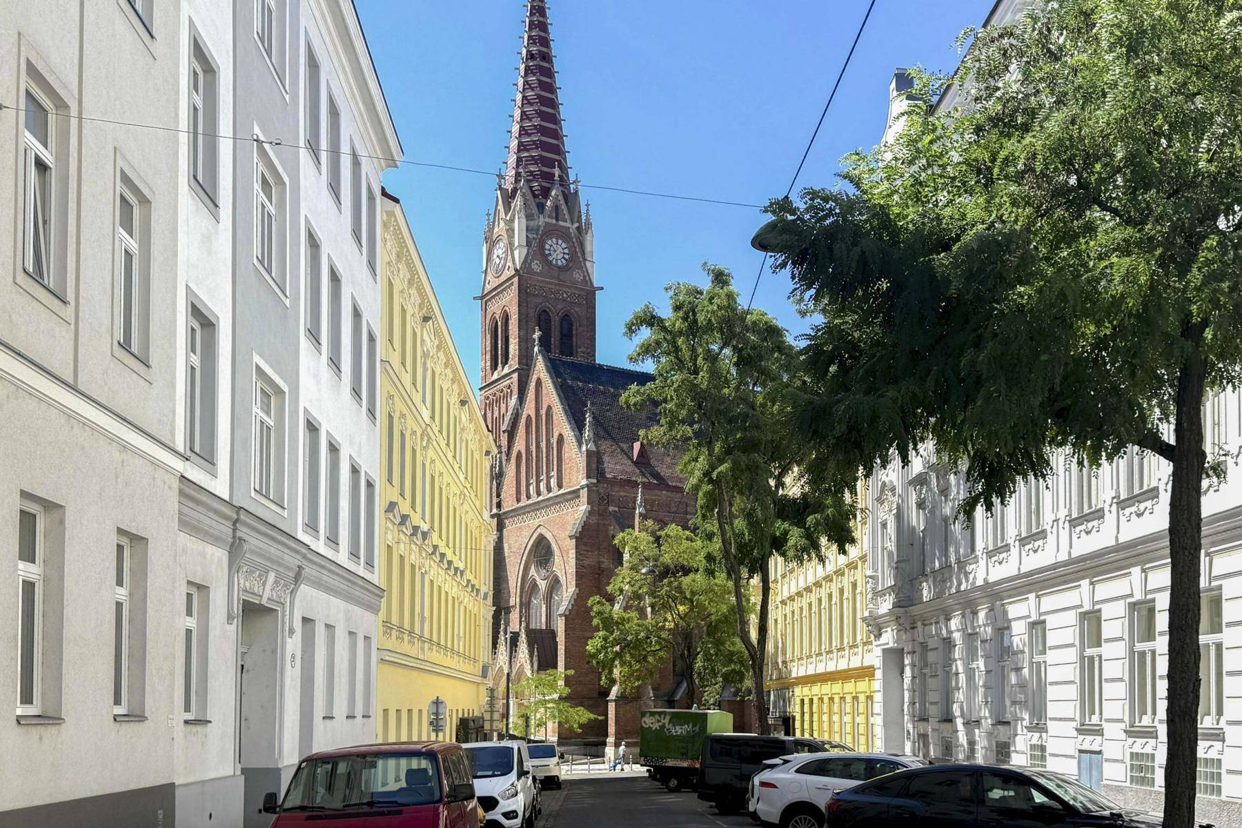 Belebte Stadtstraße mit historischen Gebäuden und einer imposanten Kirche im Hintergrund.