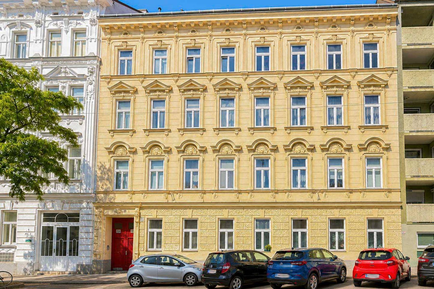 Klassische Fassade eines Altbaus mit vielen Fenstern und einer roten Eingangstür.