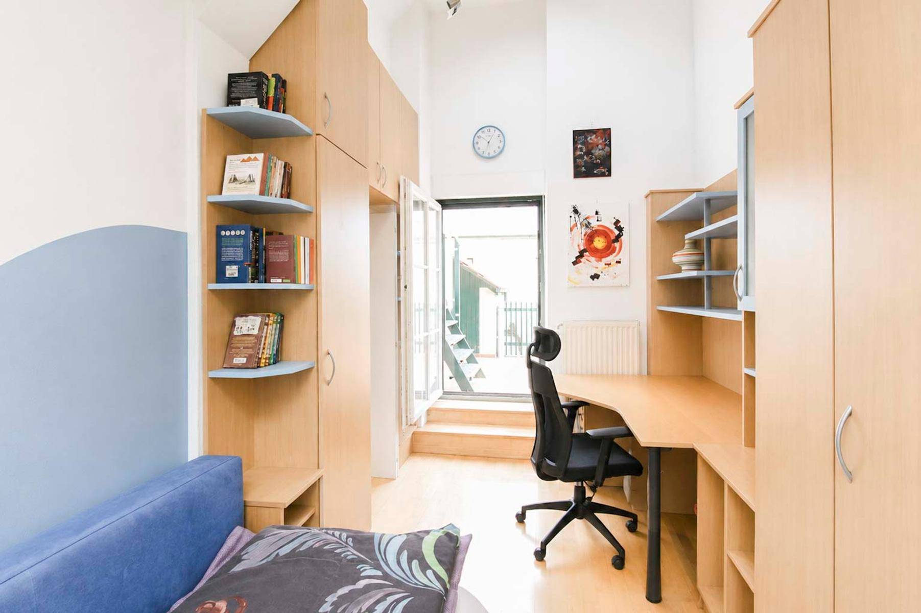 Helles Arbeitszimmer mit Schreibtisch, Bücherregalen und direktem Zugang zu einem Außenbereich.
