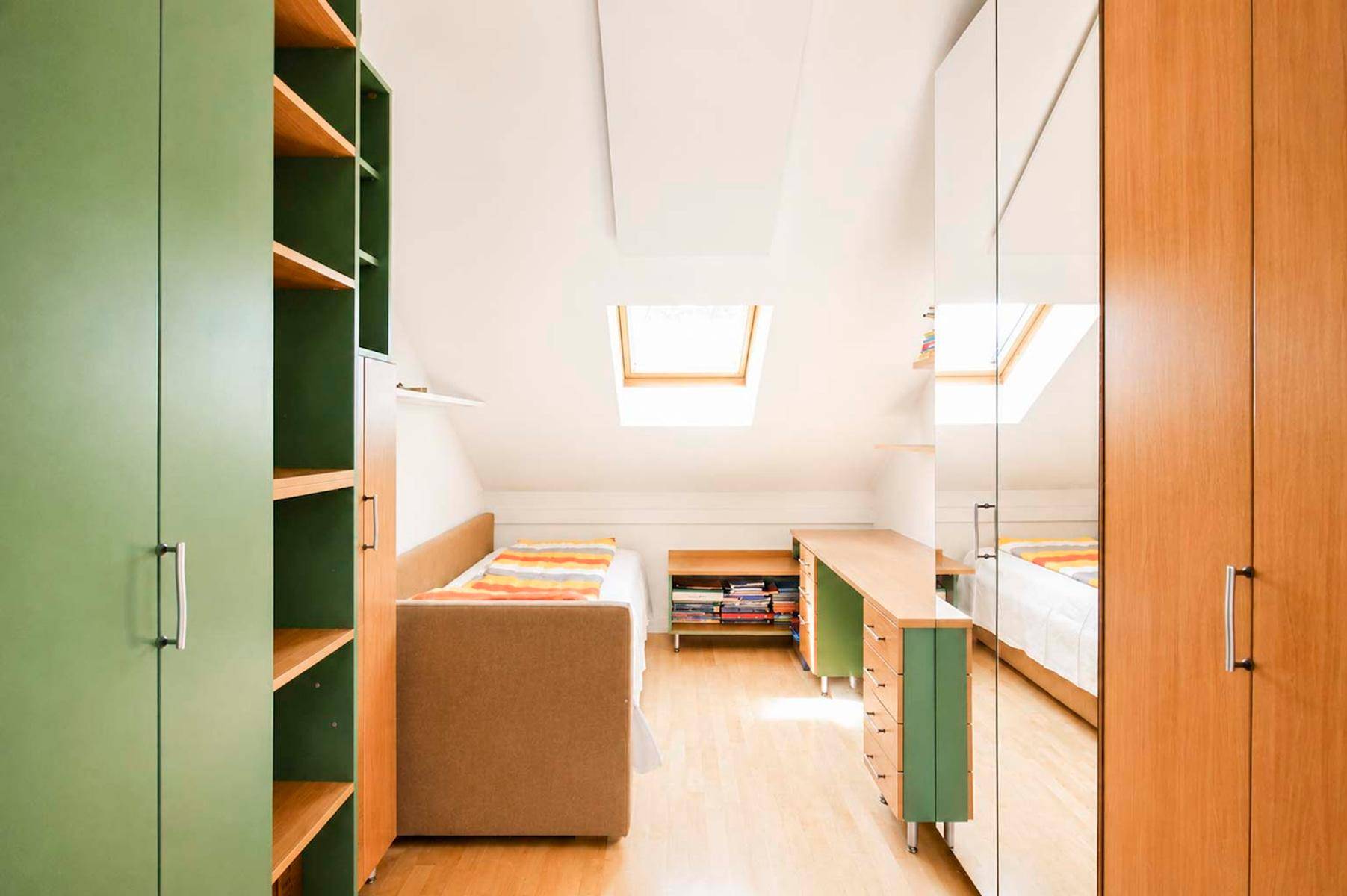 Gemütliches Dachzimmer mit Holzboden, Schreibtisch, Dachfenstern und viel Stauraum.