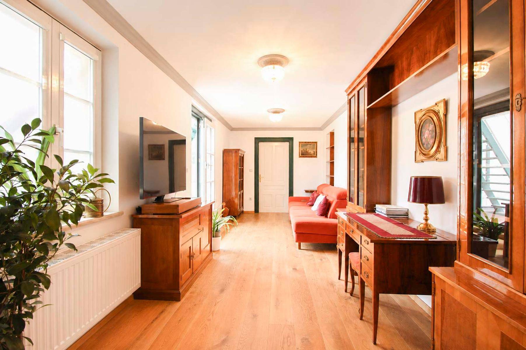 Geräumiges Wohnzimmer mit Holzboden, antiken Möbeln und großen Fenstern für viel Tageslicht.