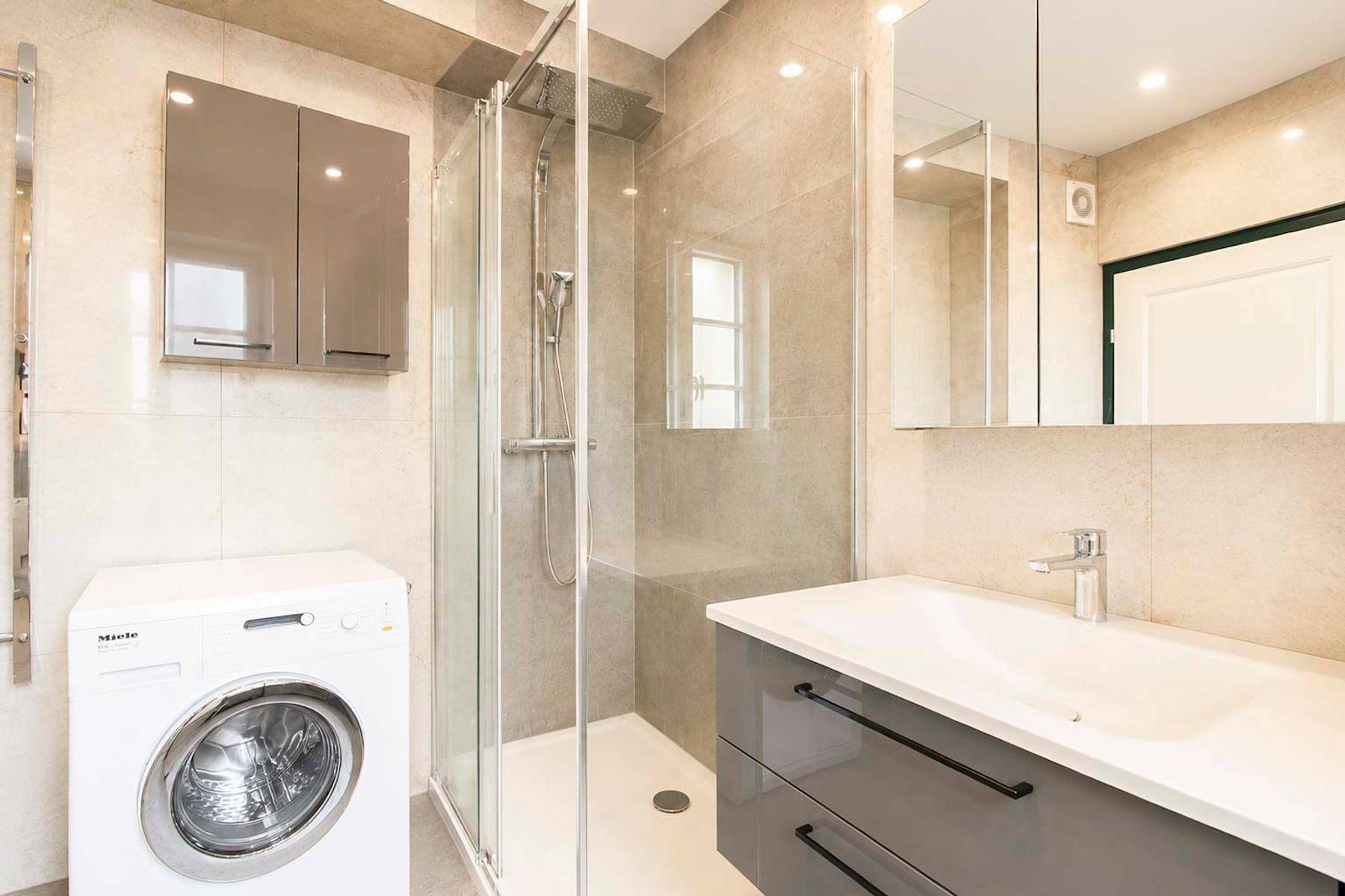 Helles Badezimmer mit Dusche, Waschmaschine, modernem Waschtisch und Handtuchheizkörper.