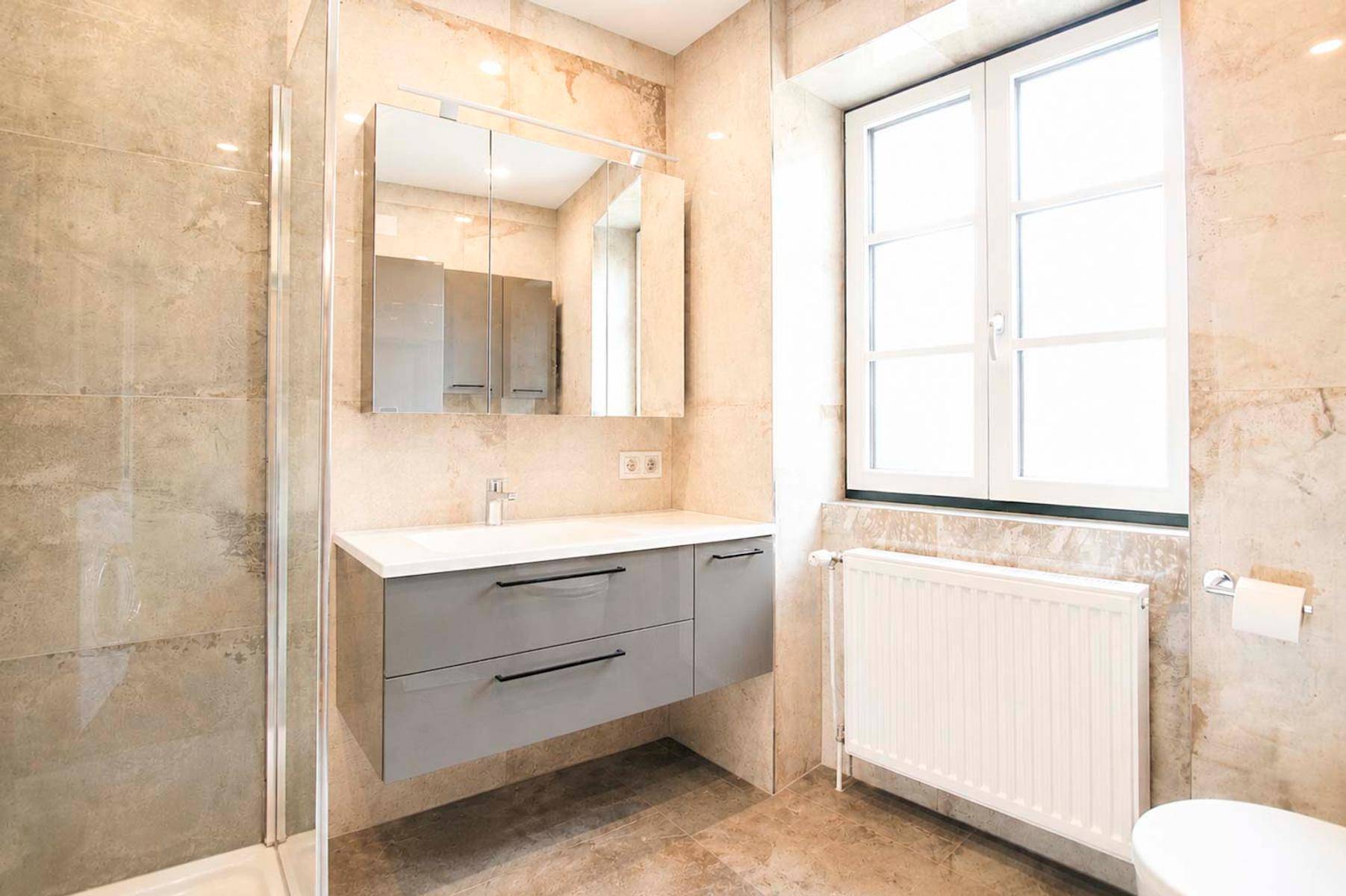 Modernes Badezimmer mit großformatigen Fliesen, Waschtisch, Spiegelschrank und Fenster.