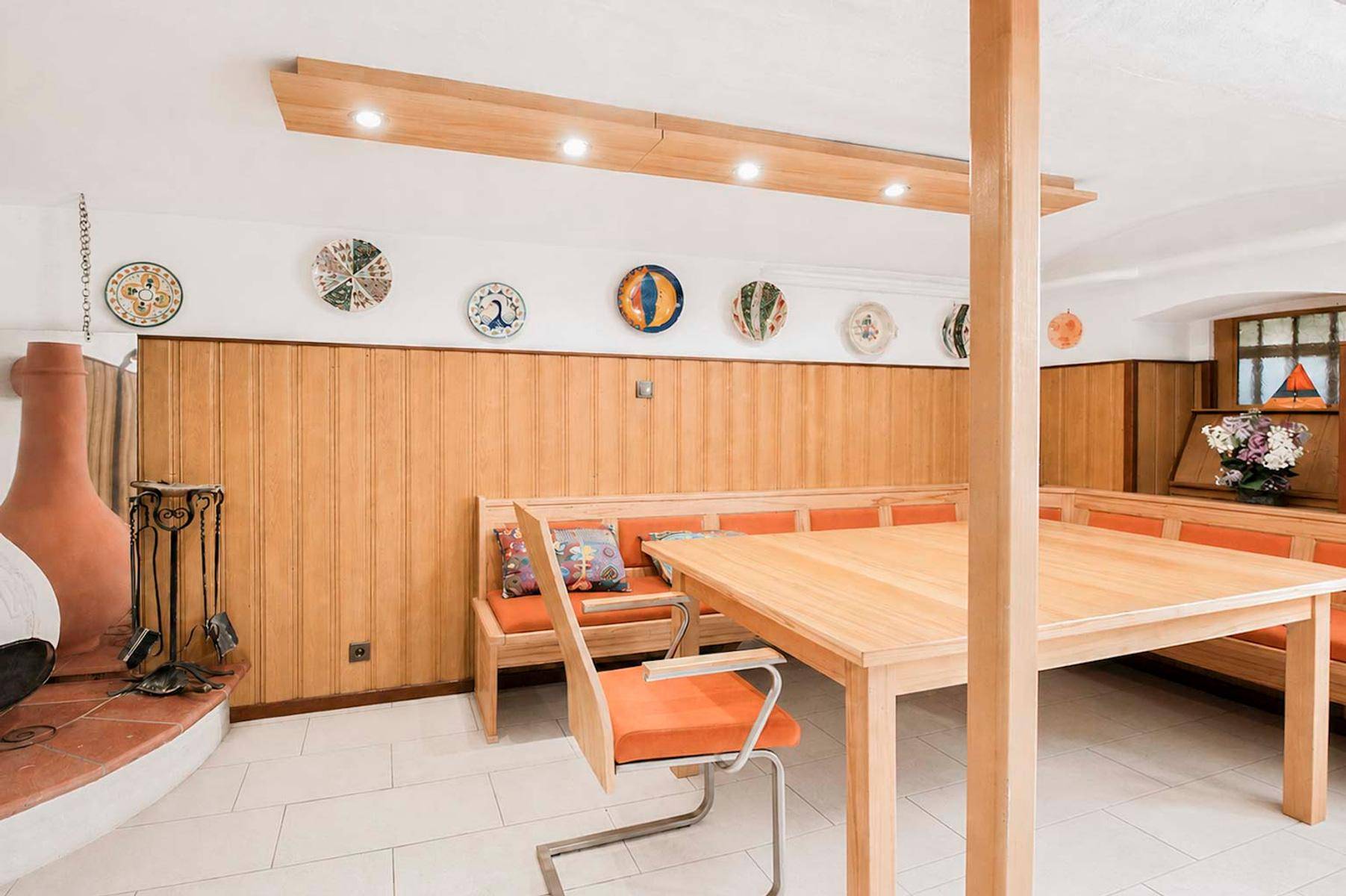 Traditioneller Essbereich mit Holztisch, Bänken und dekorativen Tellern an der Wand.