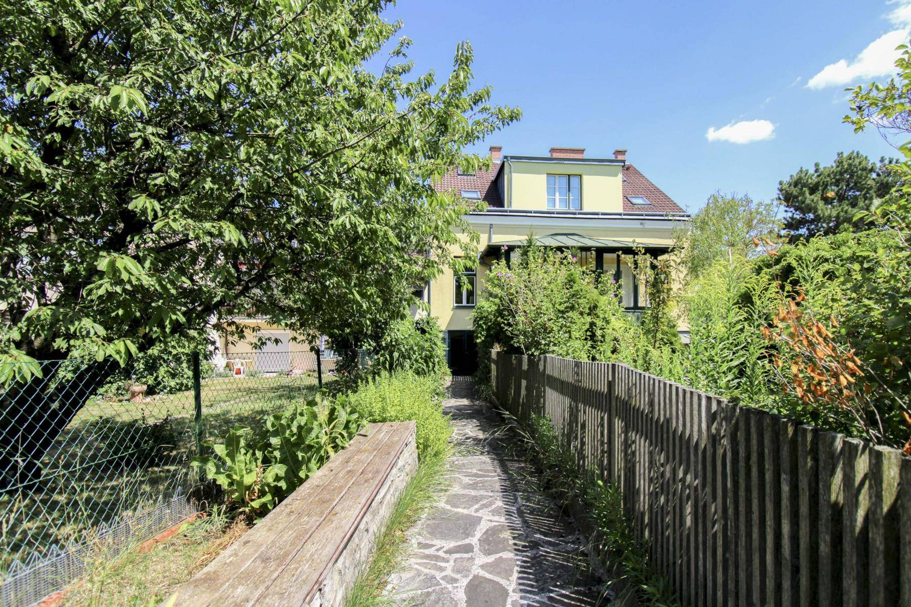 Grüner Gartenweg führt zu einem charmanten Haus unter blauem Himmel und Bäumen.