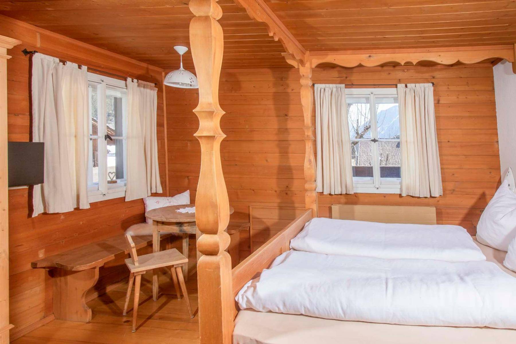 Gemütliches Schlafzimmer im Landhausstil mit Holzwänden, Himmelbett und einem kleinen Esstisch am Fenster.