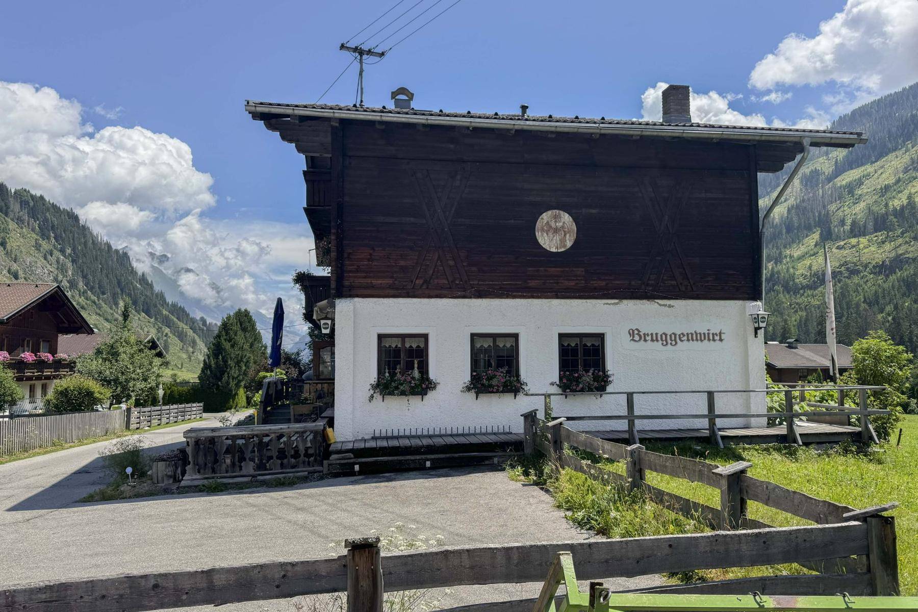 Seitenansicht des traditionellen Holzhauses mit weißer Fassade und Holzbalkonen, eingebettet in eine Berglandschaft.