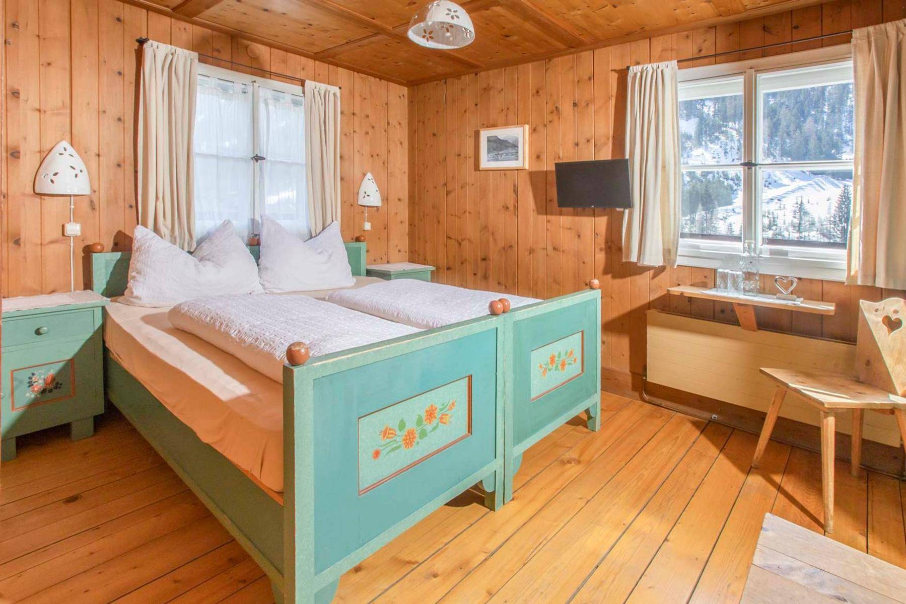 Rustikales Schlafzimmer mit Holzwänden, zwei Einzelbetten im Landhausstil und Blick auf die verschneiten Berge.