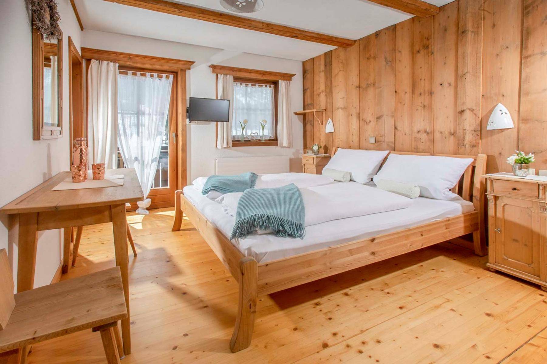 Komfortables Schlafzimmer mit Holzboden und -wänden, Doppelbett und einem kleinen Schreibtisch am Fenster.