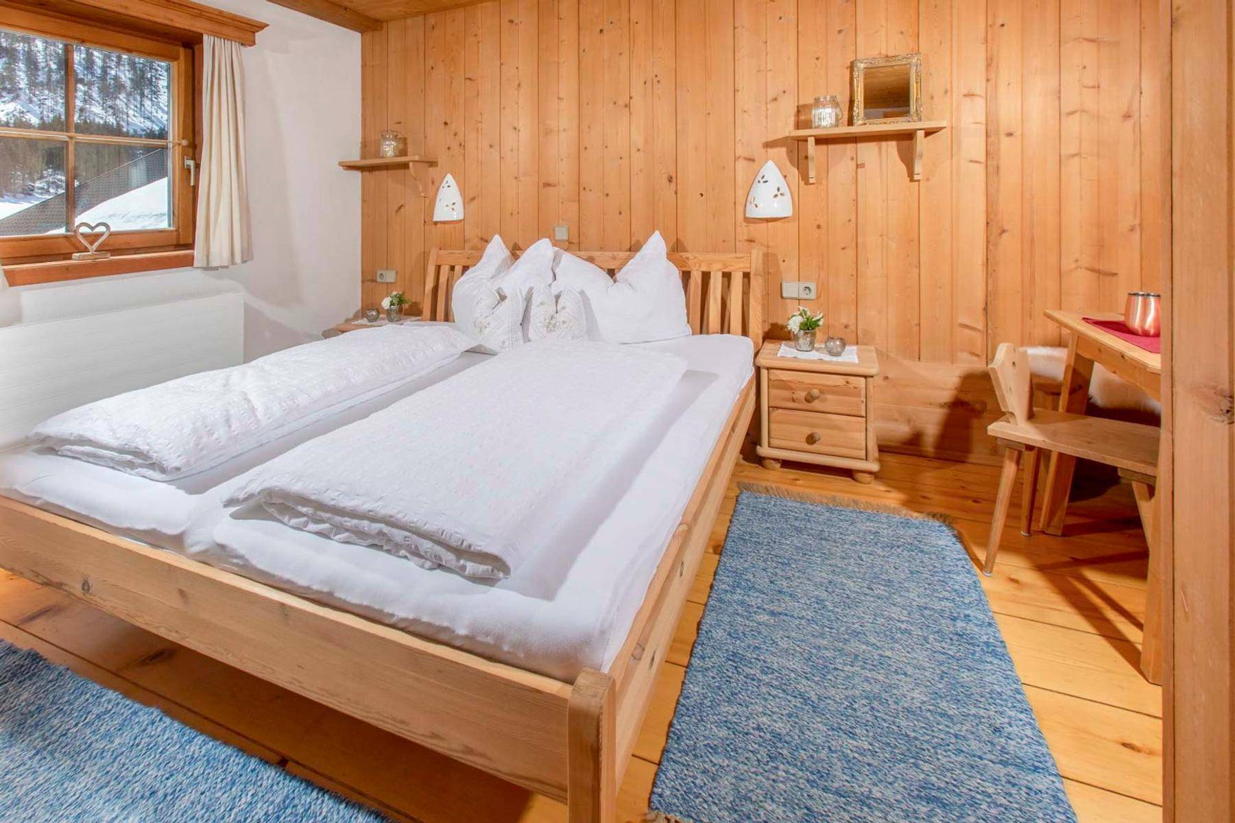 Gemütliches Schlafzimmer mit Holzwänden und -boden, Doppelbett und einem blauen Teppich, mit Bergblick.