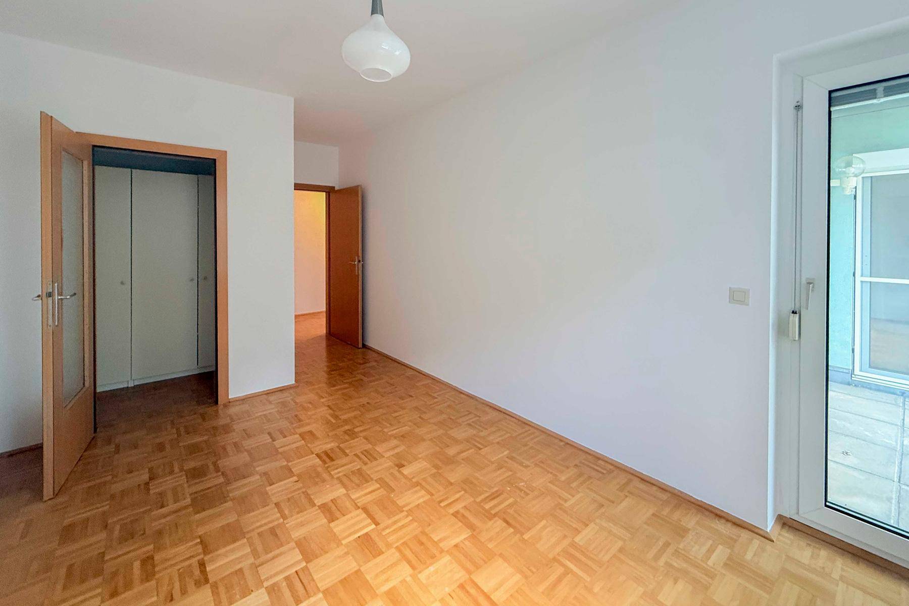 Schlafzimmer mit Parkettboden und Zugang zu einem Balkon oder einer Terrasse, hell und einladend.