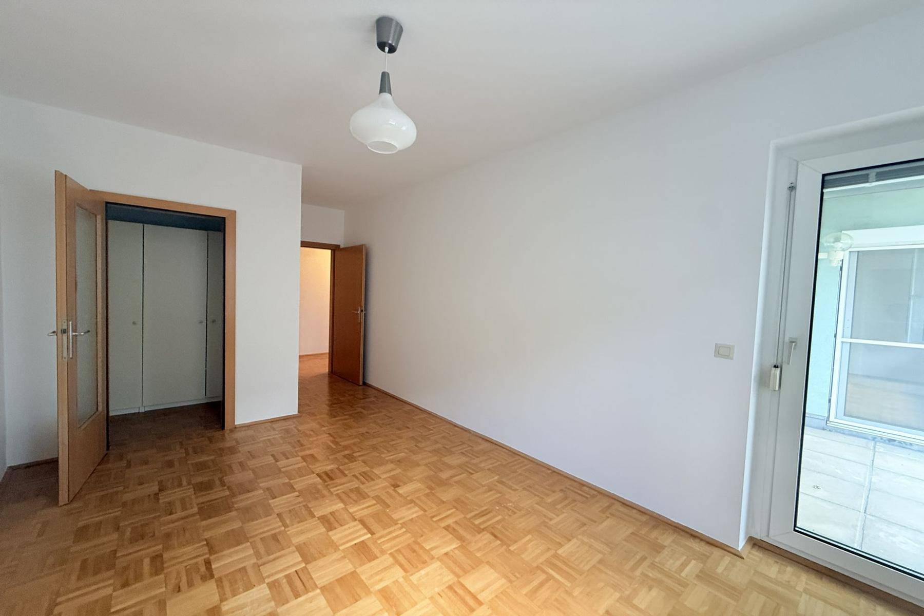 Schlafzimmer mit Parkettboden und Zugang zu einem Außenbereich, ideal als Gäste- oder Kinderzimmer.