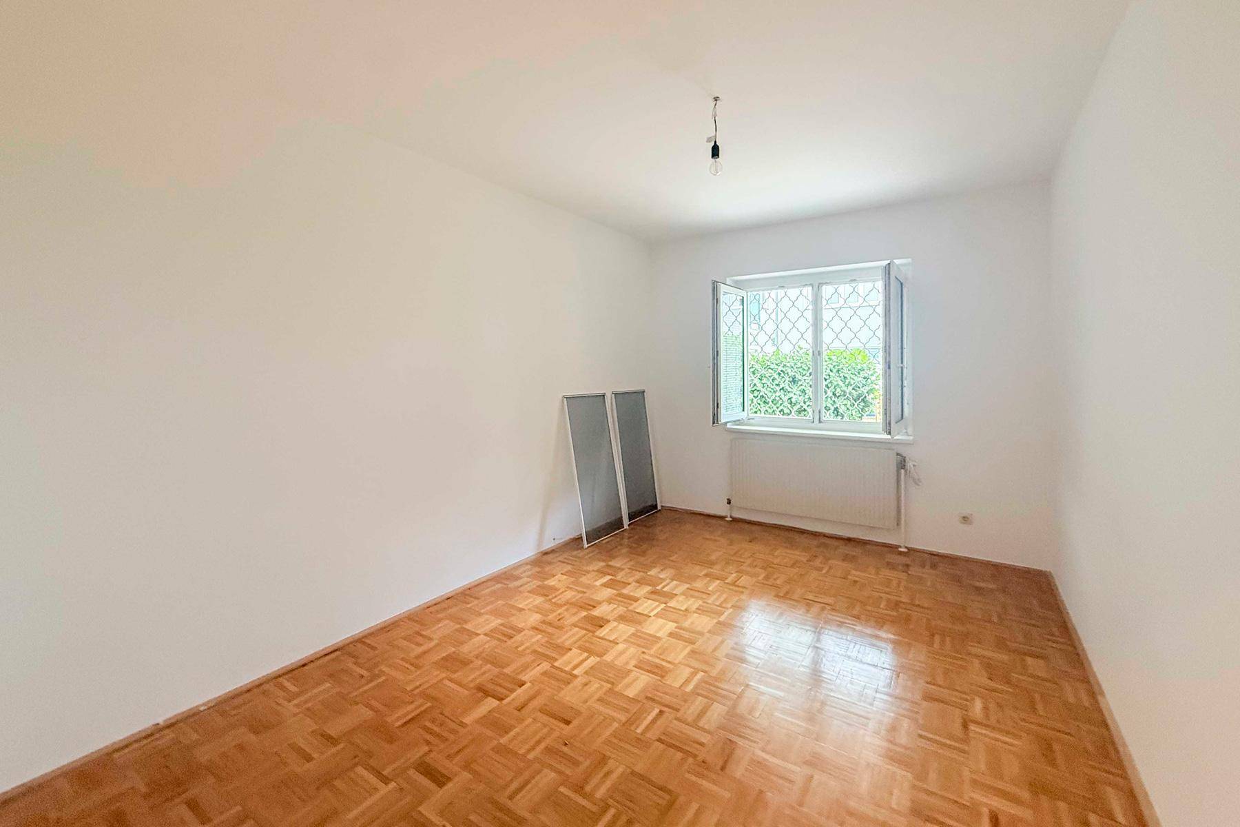 Schlafzimmer mit Parkettboden und Fenster zum begrünten Außenbereich, bietet Ruhe und Privatsphäre.