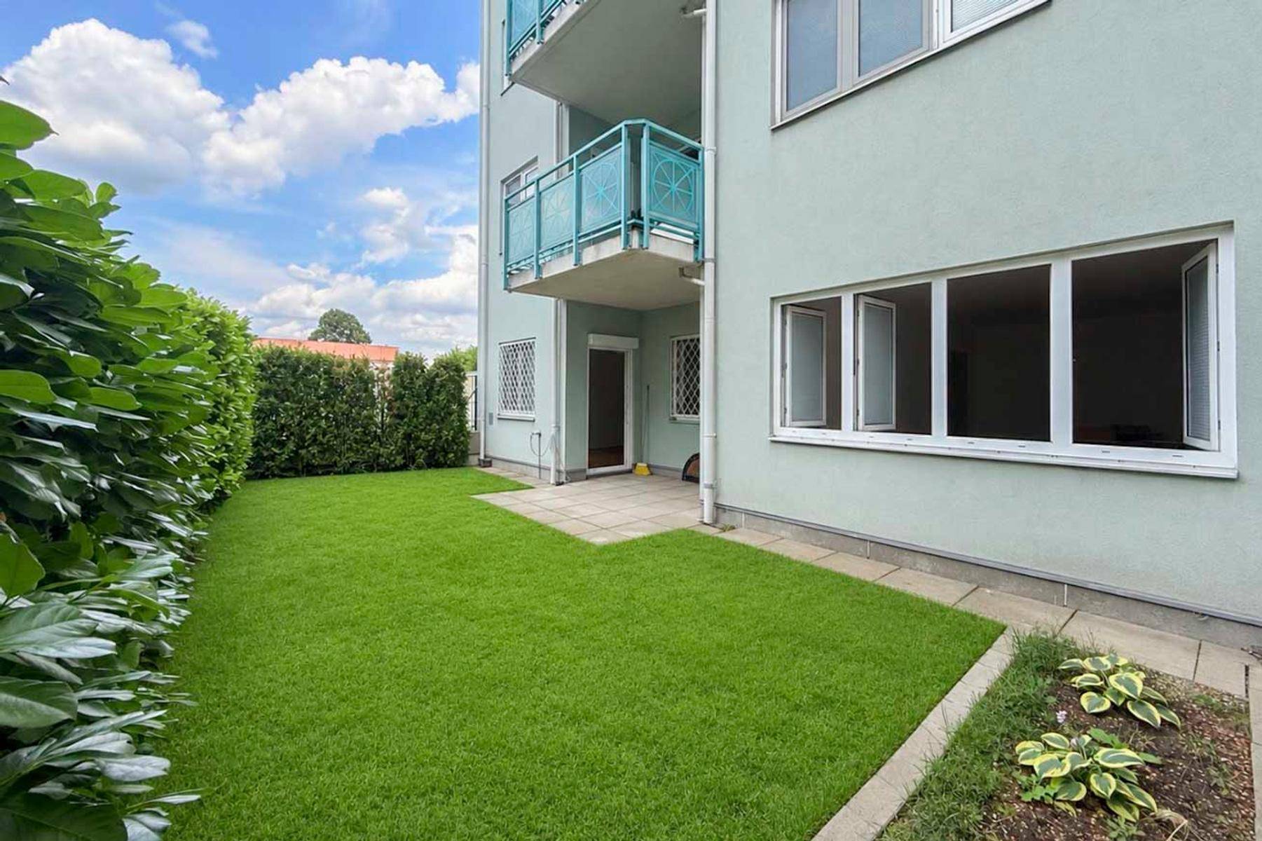 Seitlicher Gartenbereich mit Rasen, Hecke und Zugang zu einer kleinen Terrasse, ideal zum Entspannen.