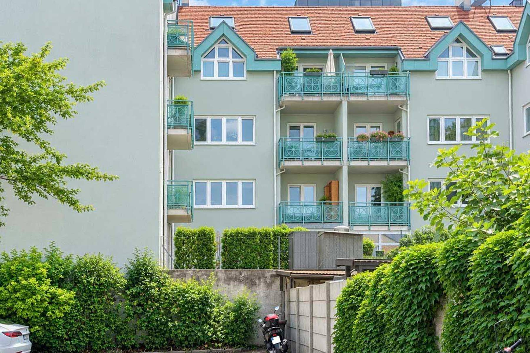 Mehrstöckiges Wohngebäude mit Balkonen, grüner Fassade und rotem Ziegeldach unter blauem Himmel.