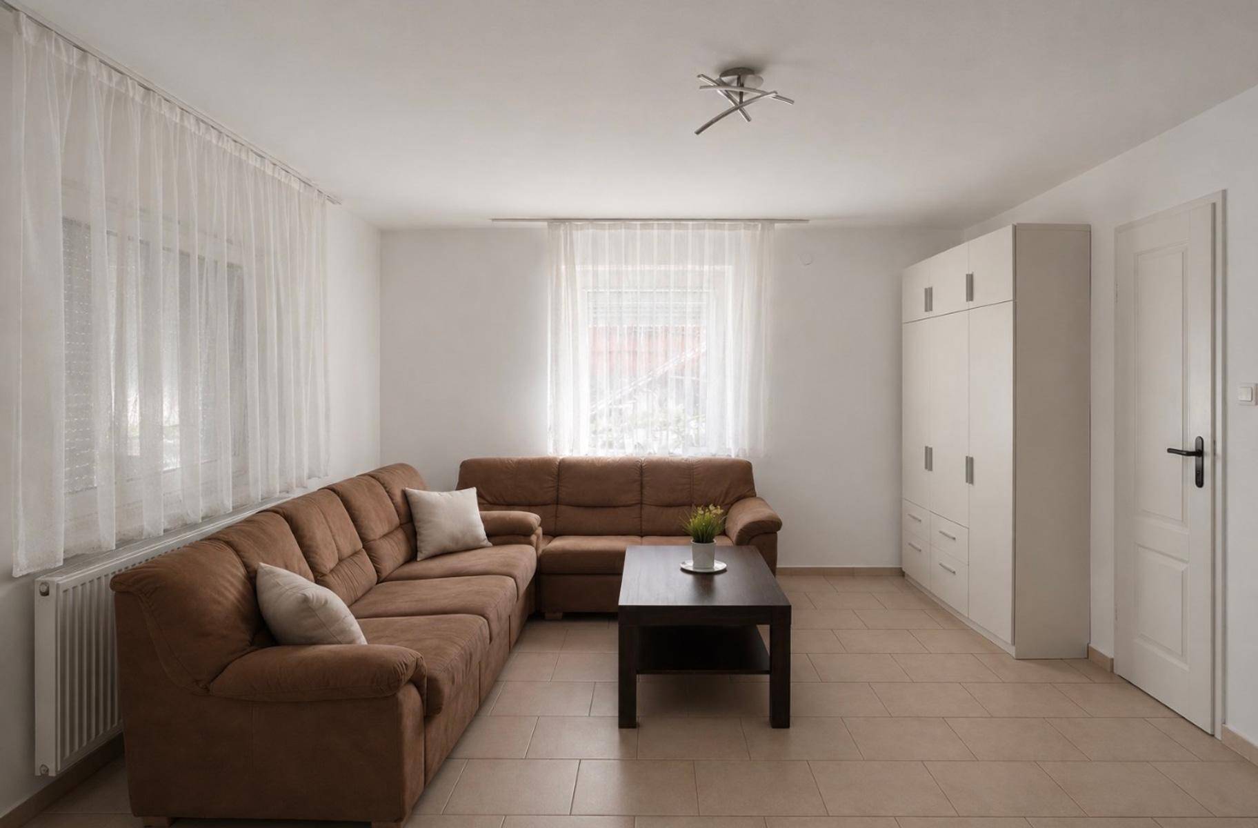 Gemütliches Wohnzimmer mit braunem Ecksofa, weißem Schrank und hellem Fliesenboden.